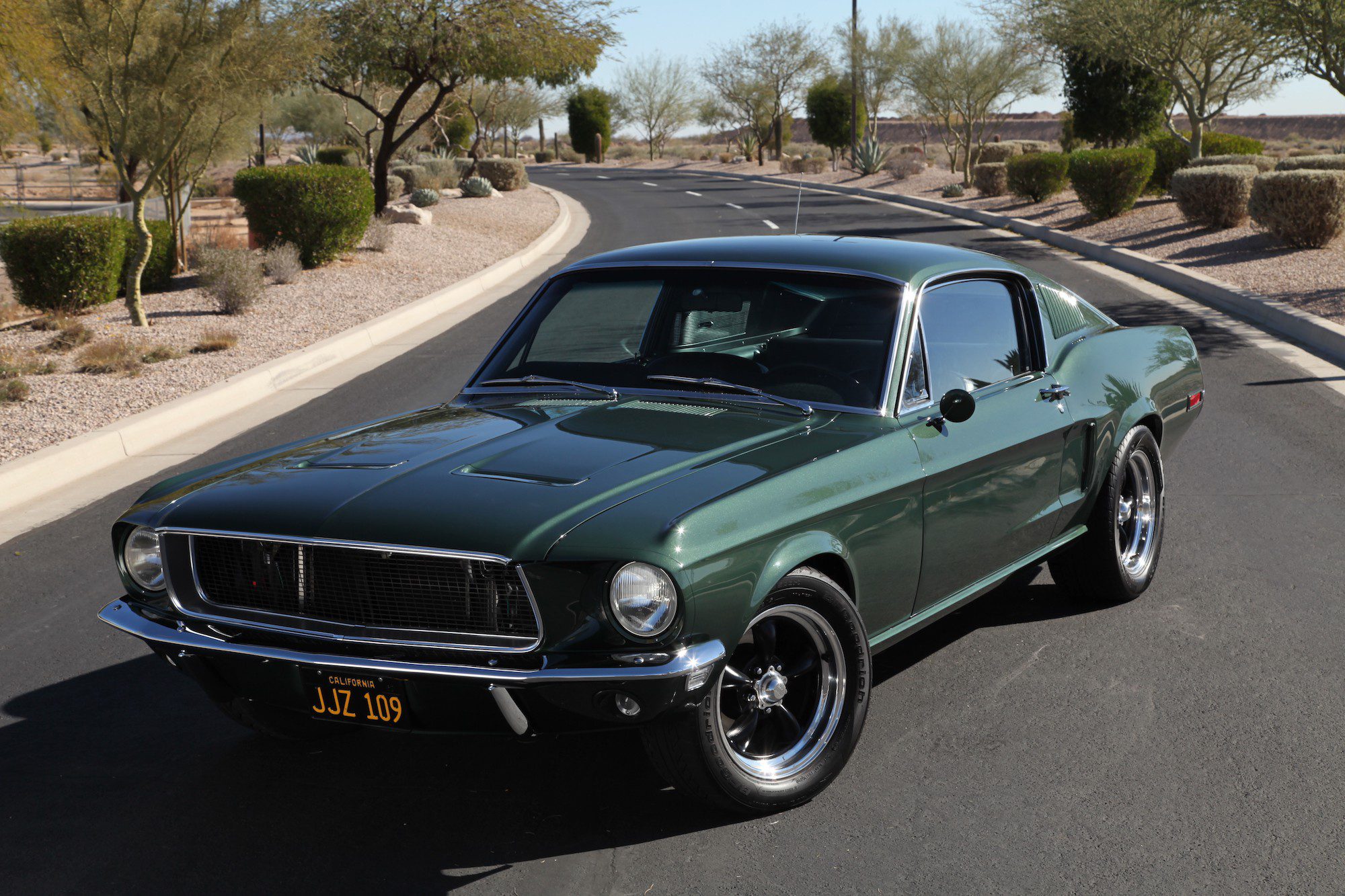 Classic dark green 1967 Ford Mustang driving on a sunny road.