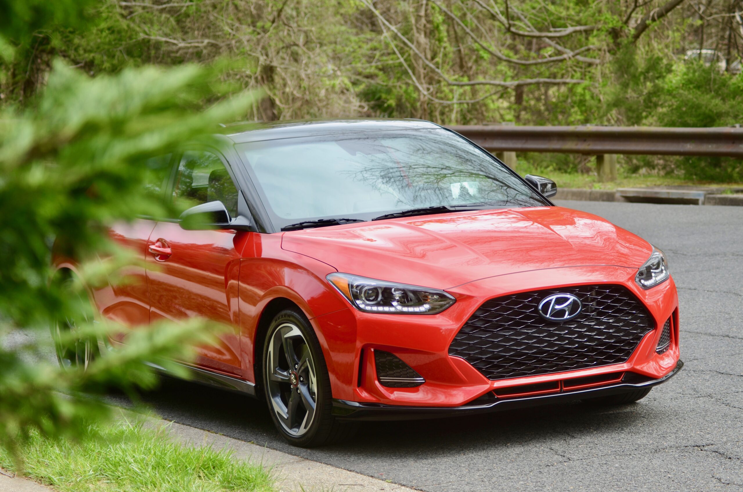 Red Hyundai convertible car parked outdoors with greenery in the background.