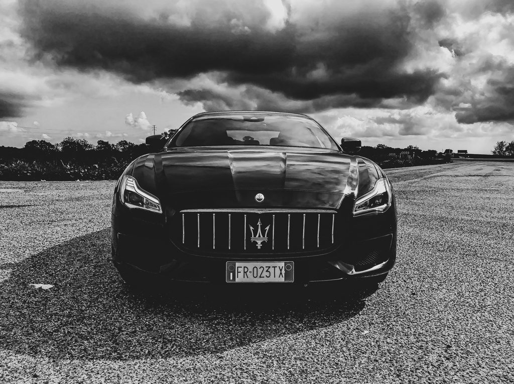 Black Maserati parked under dramatic cloudy sky.