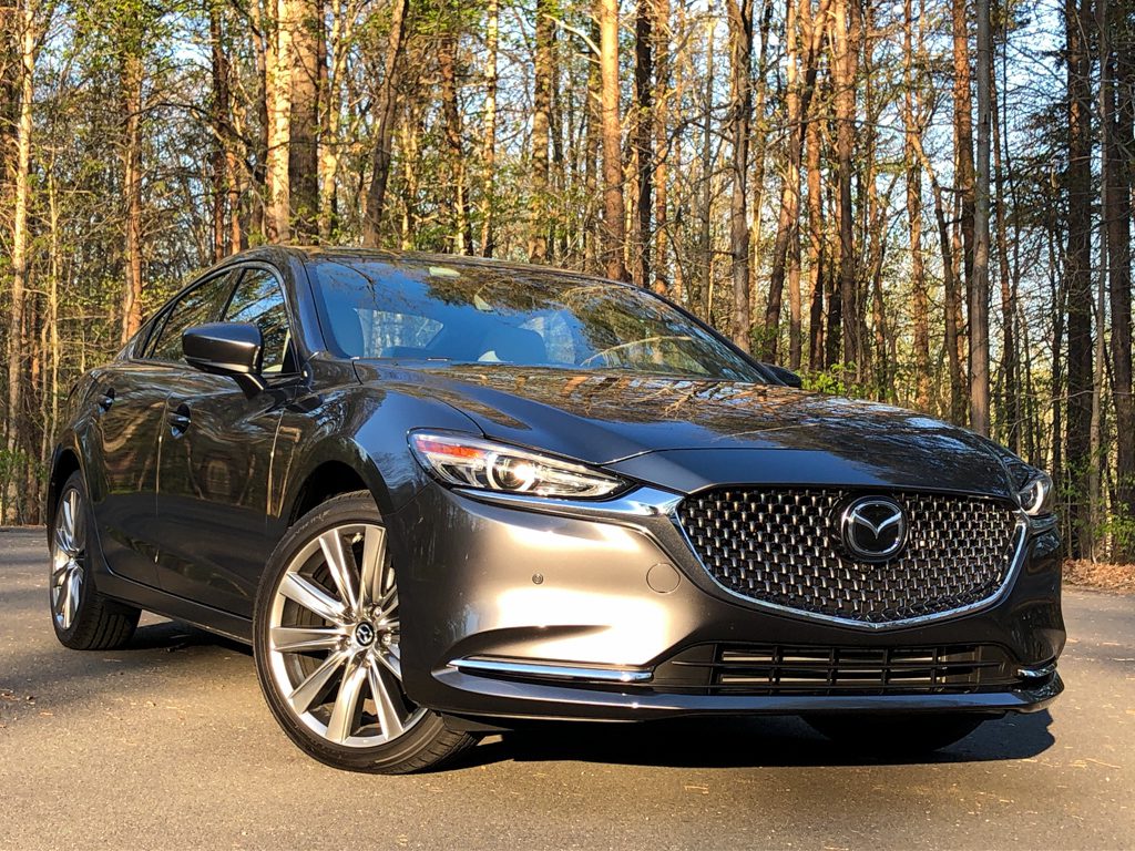 Sleek silver Mazda parked on a forest road with autumn foliage.