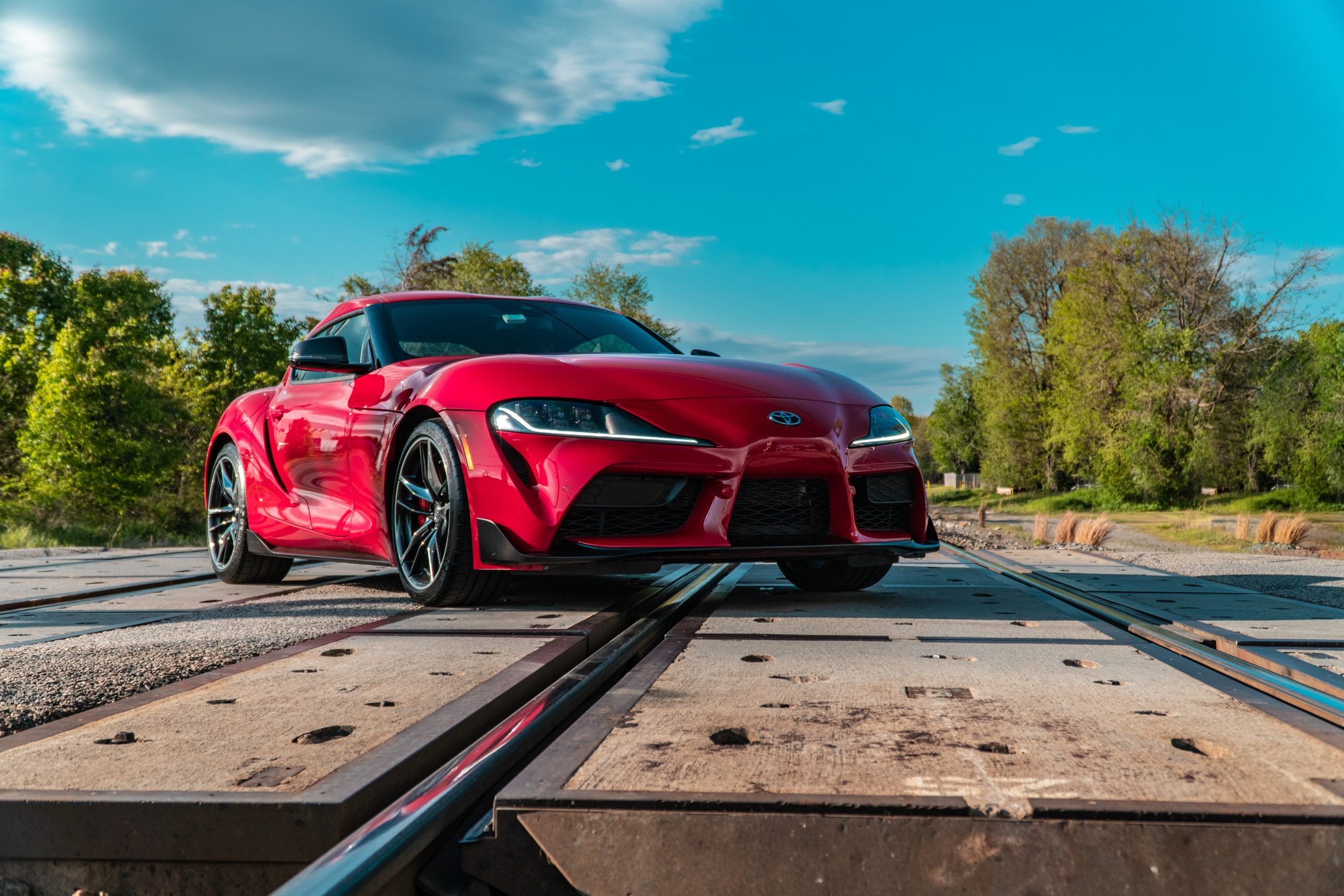 Red sports car crossing railroad tracks under a clear blue sky.