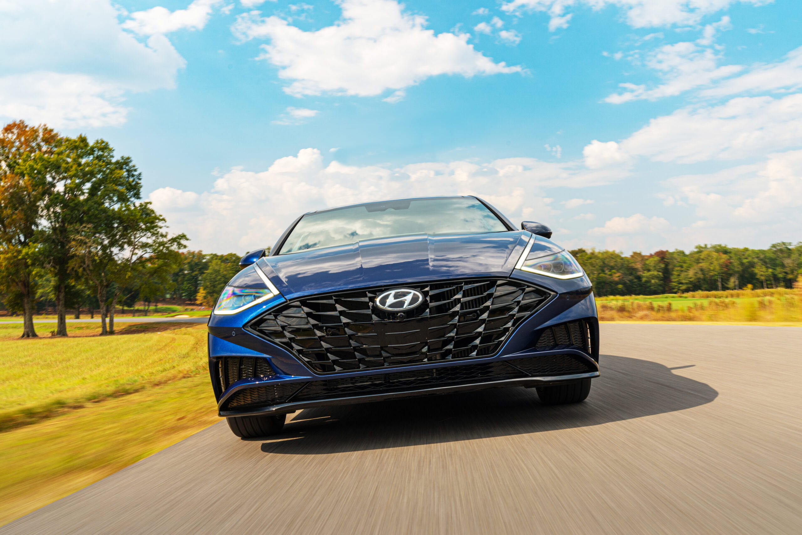 Sleek black Hyundai car driving on a sunny road with a blue sky.