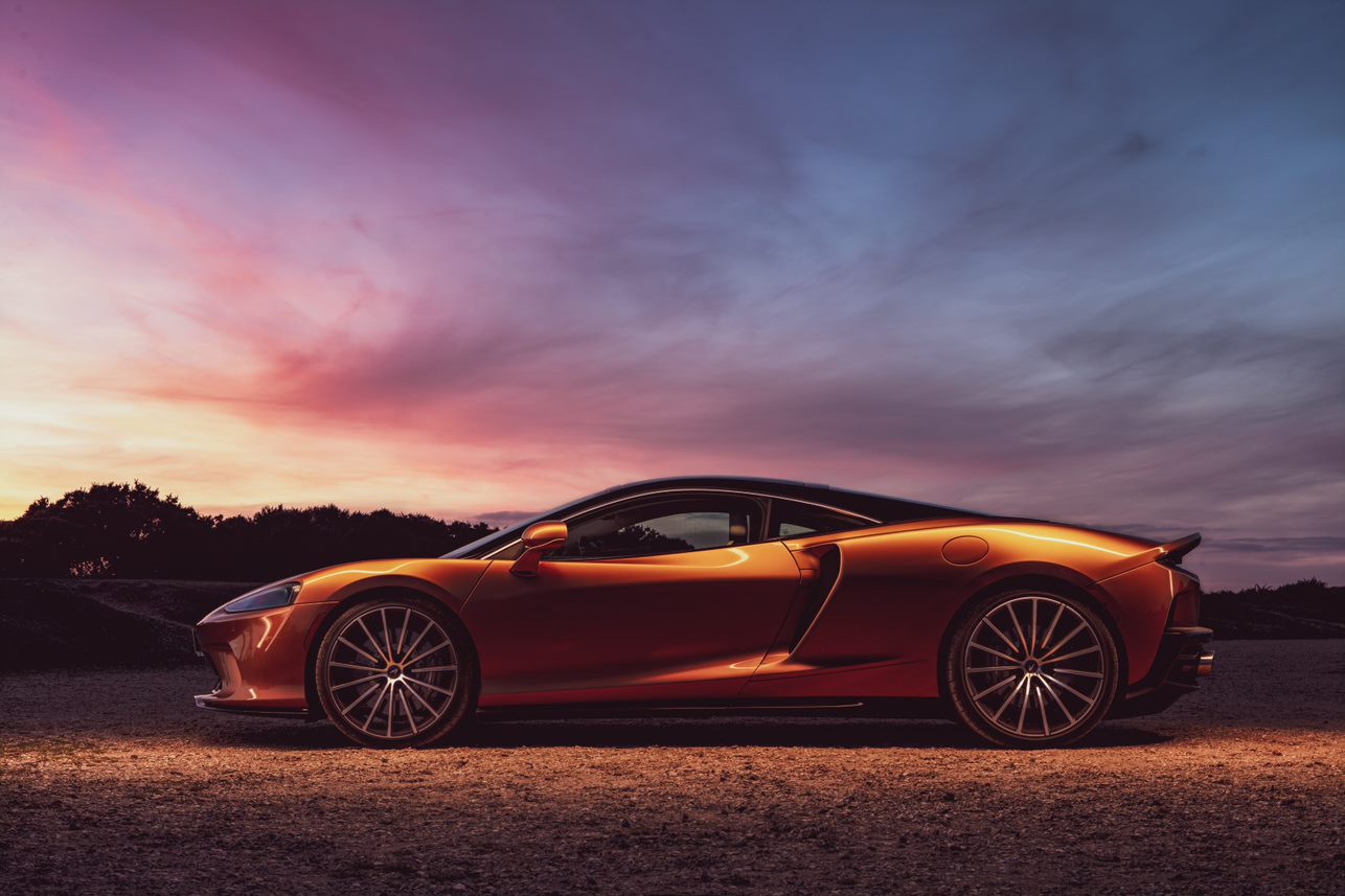 Luxury sports car parked at sunset with a colorful sky.