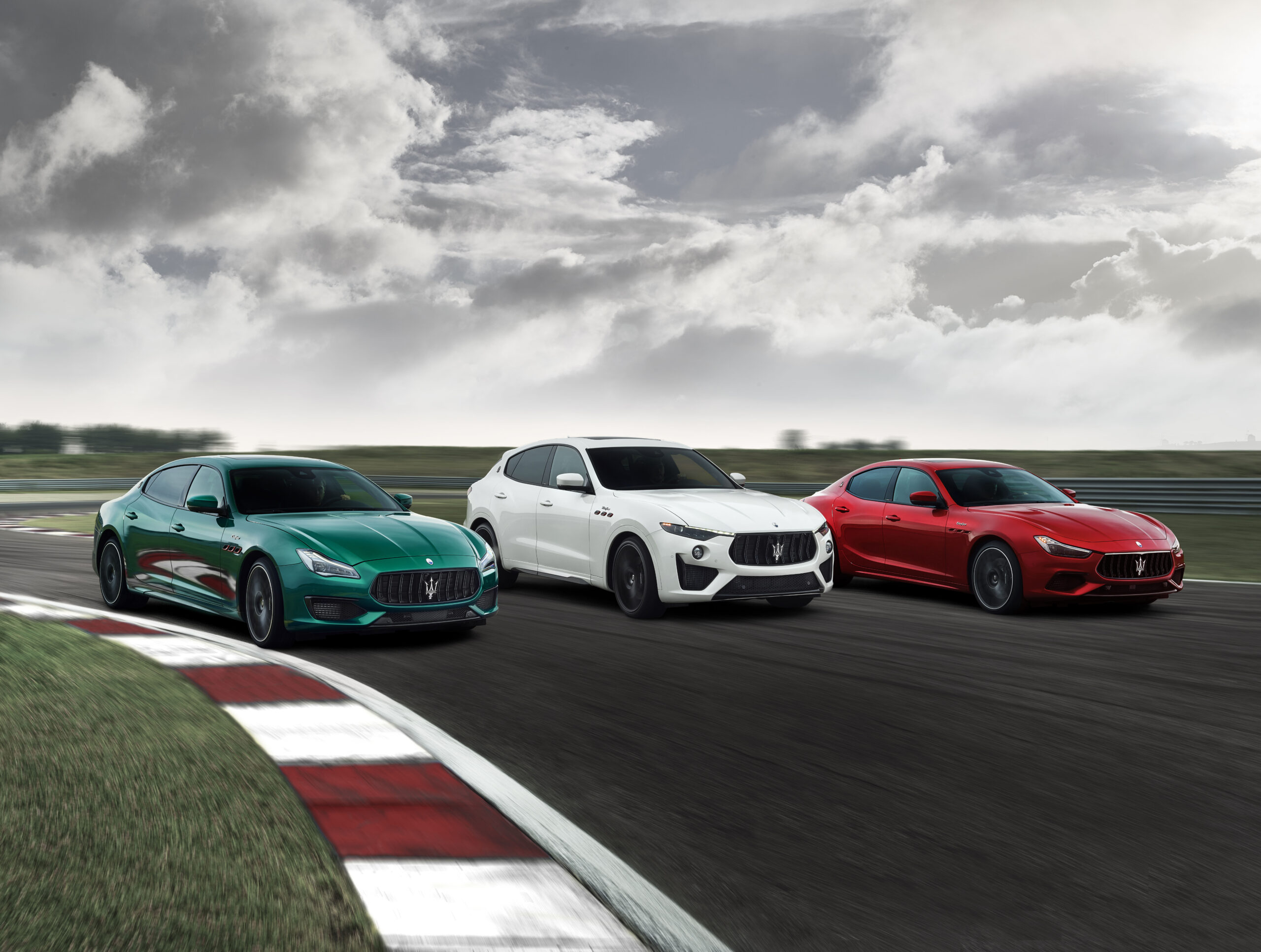 Three sporty cars racing on a track under a cloudy sky.