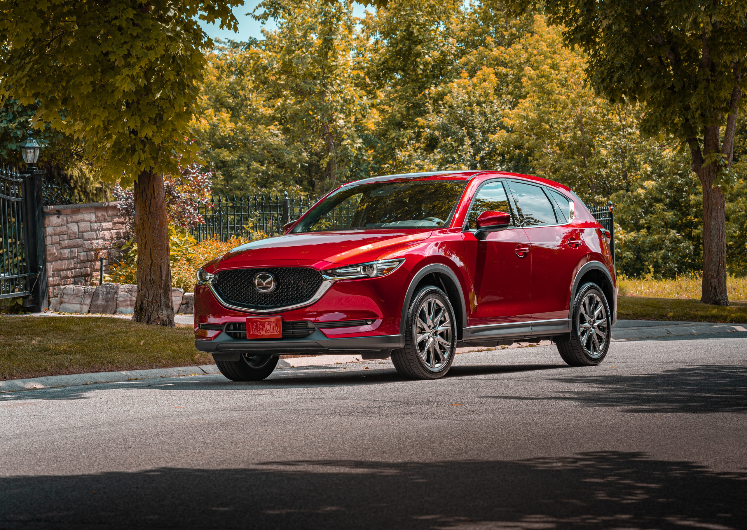 Red Mazda CX-5 SUV parked on a tree-lined street.
