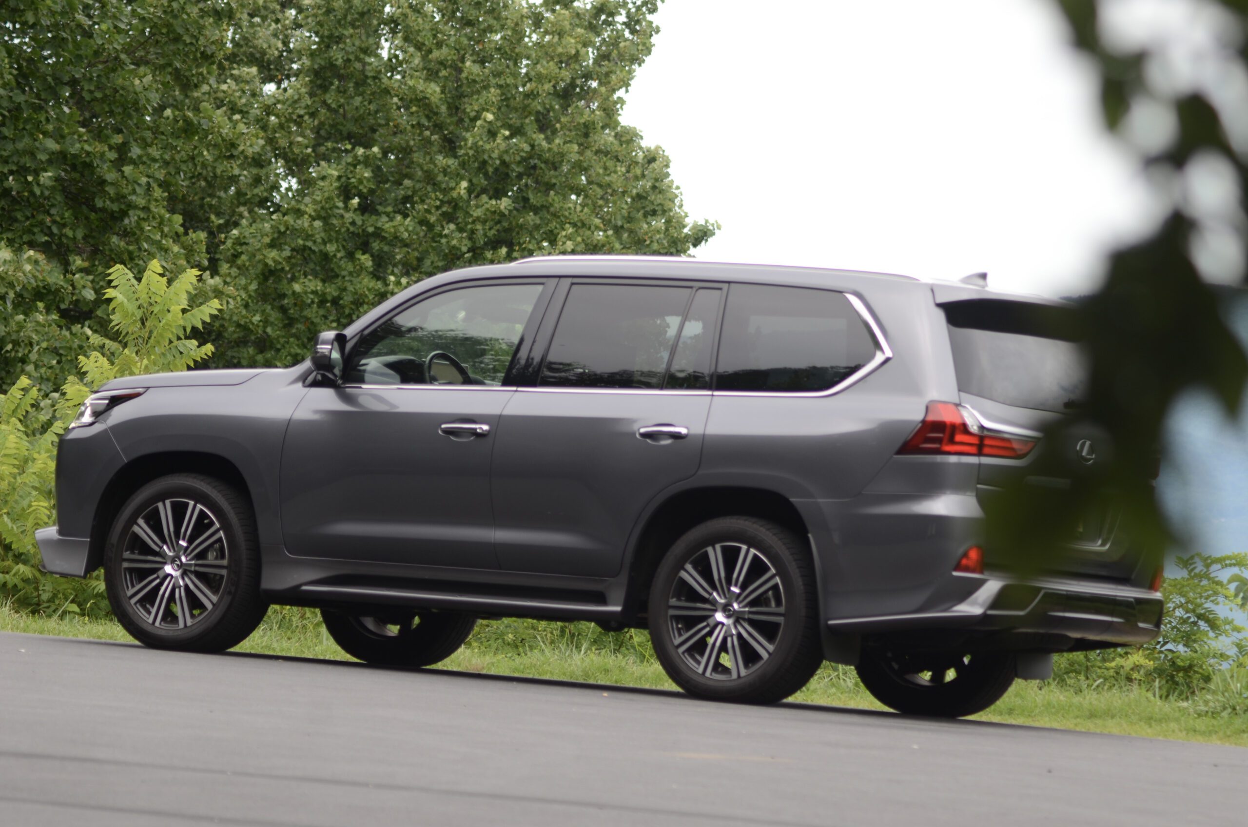 Gray luxury SUV parked on pavement with greenery in background.