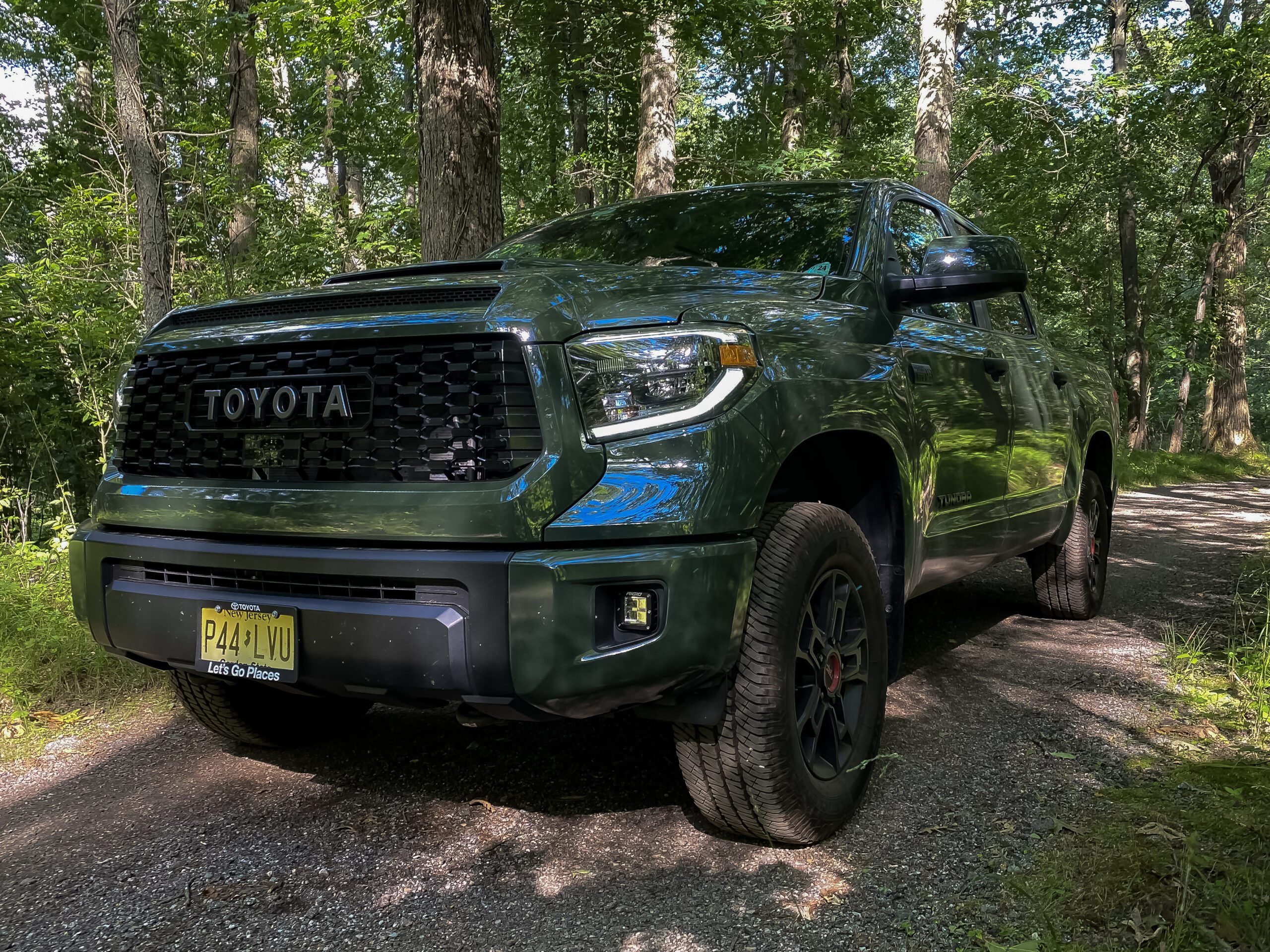 Green Toyota pickup truck parked on a forest trail under trees.