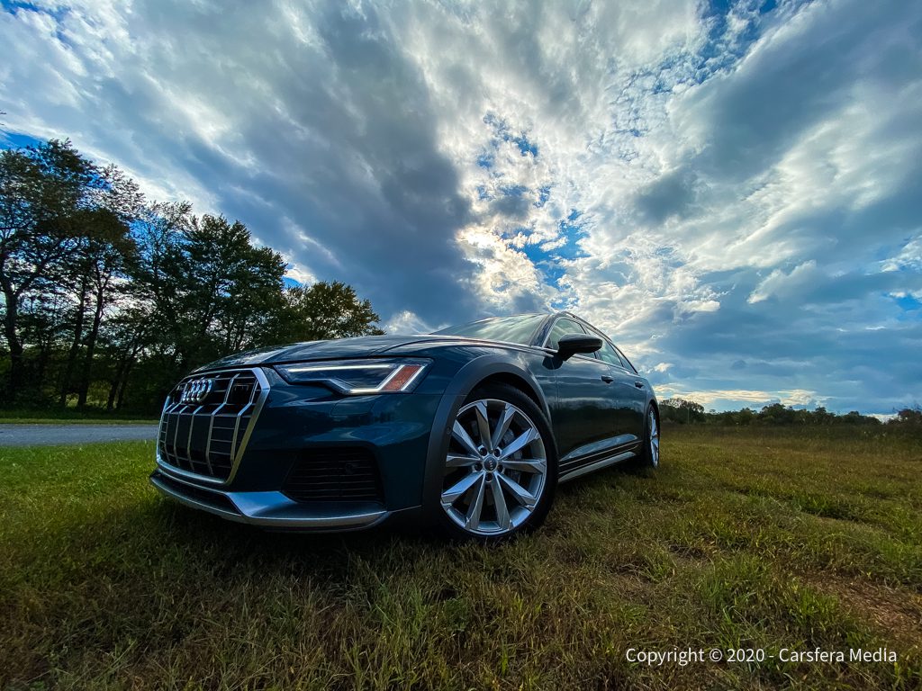 A sleek black car parked on grass under a dramatic cloudy sky.