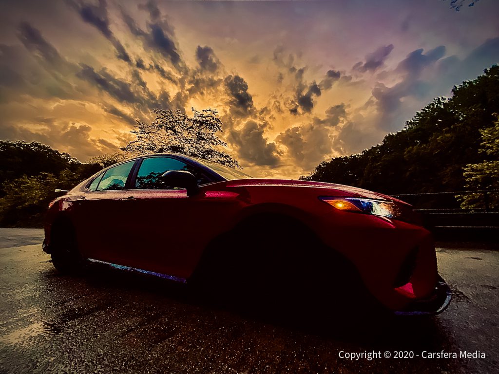 Red sports car parked under a dramatic sunset sky.