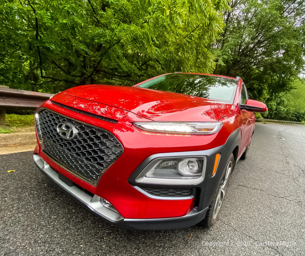 A red Hyundai Kona parked on a road surrounded by greenery.