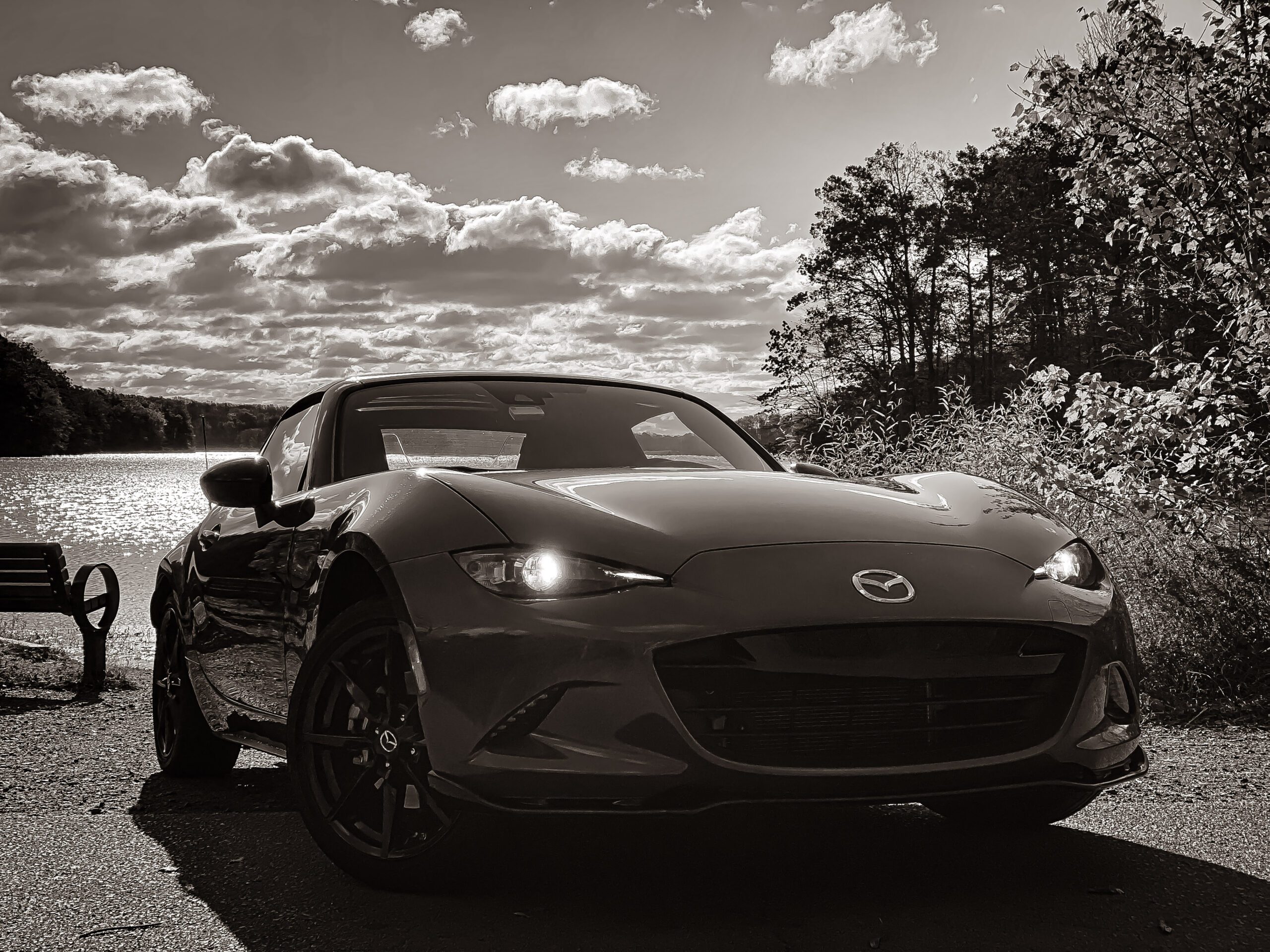 A sleek Mazda convertible on a scenic road under a dramatic sky.