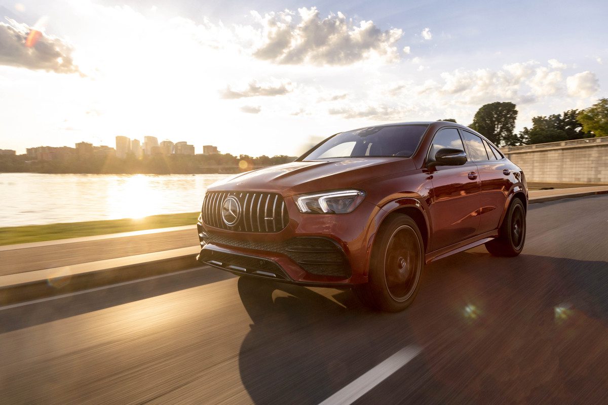 A red luxury SUV driving on a city road at sunset.