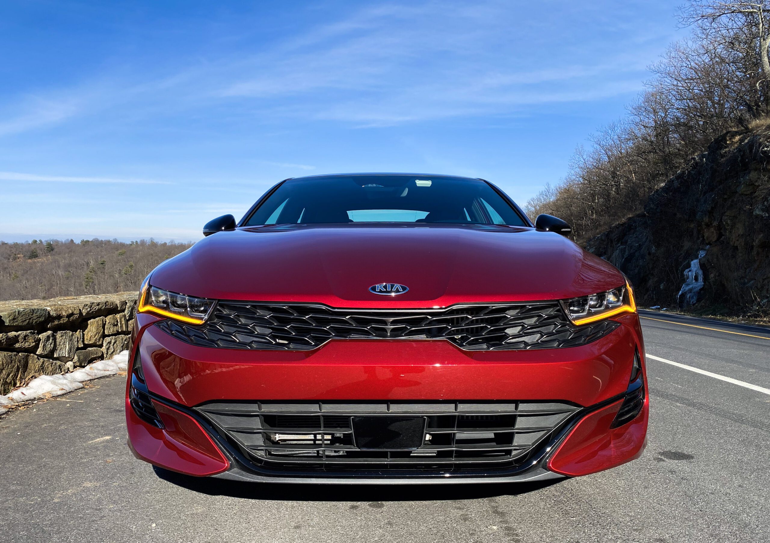 Front view of a sleek red Kia car under clear blue sky.