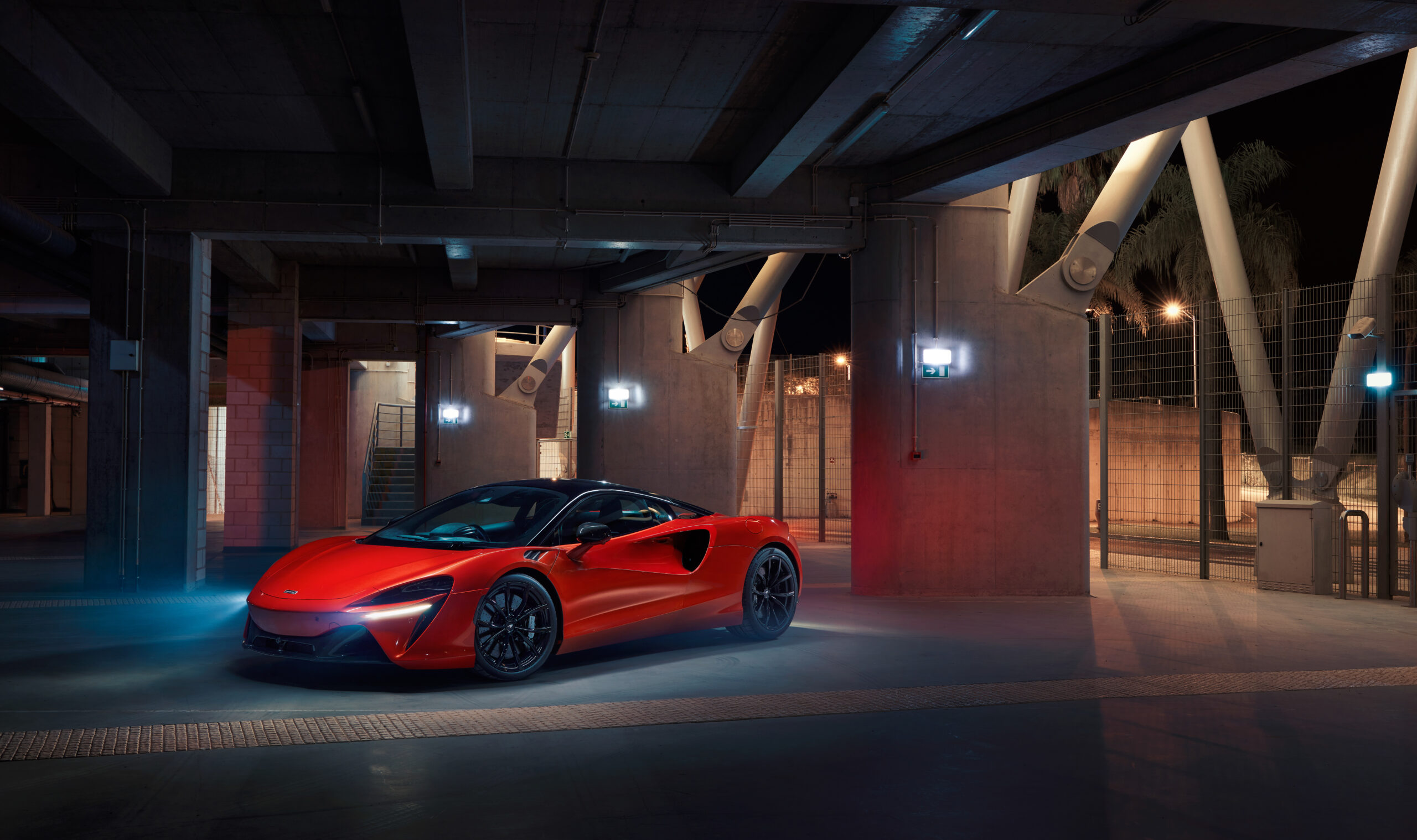 A red sports car parked in an industrial-style garage with dramatic lighting.