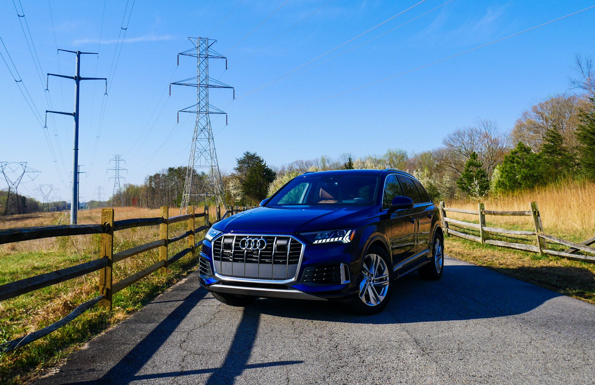 A blue Audi SUV parked on a sunny road beside a wooden fence.