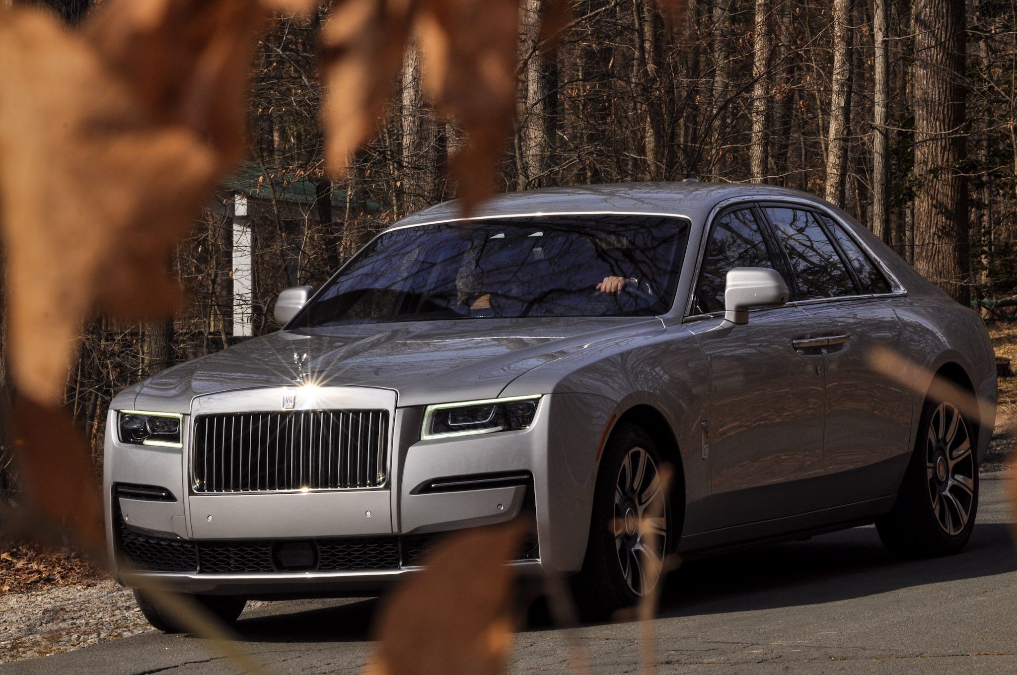 A silver luxury Rolls-Royce car parked on a street with autumn leaves in the foreground.