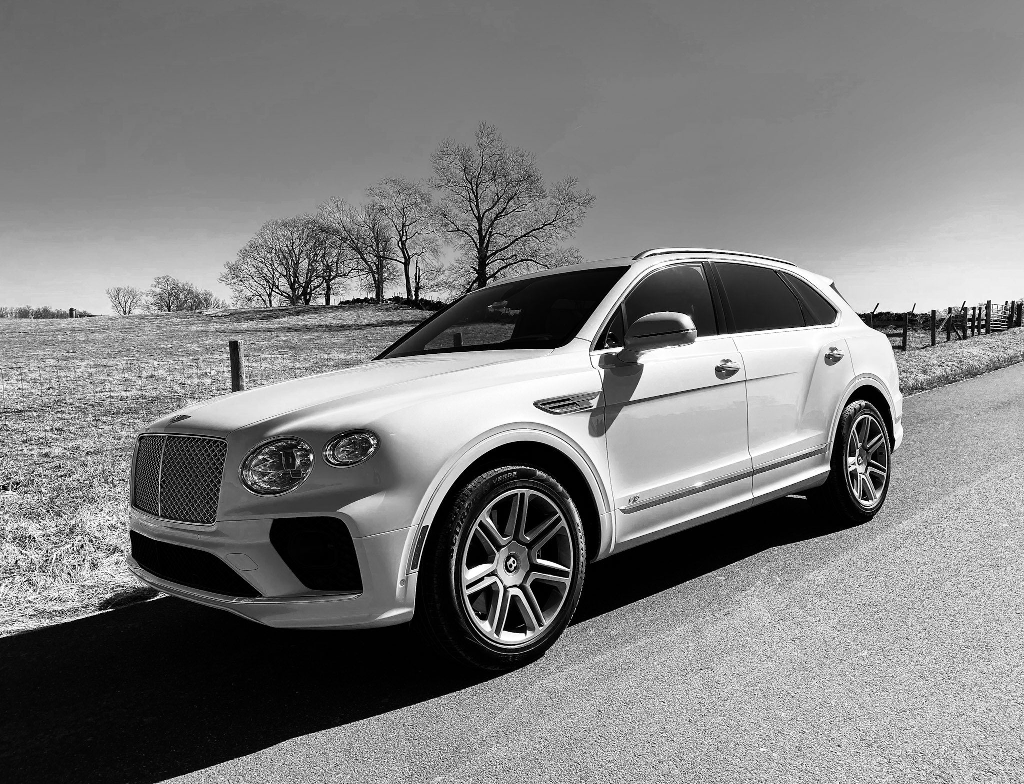 Black and white photo of a luxury SUV on a sunny road.