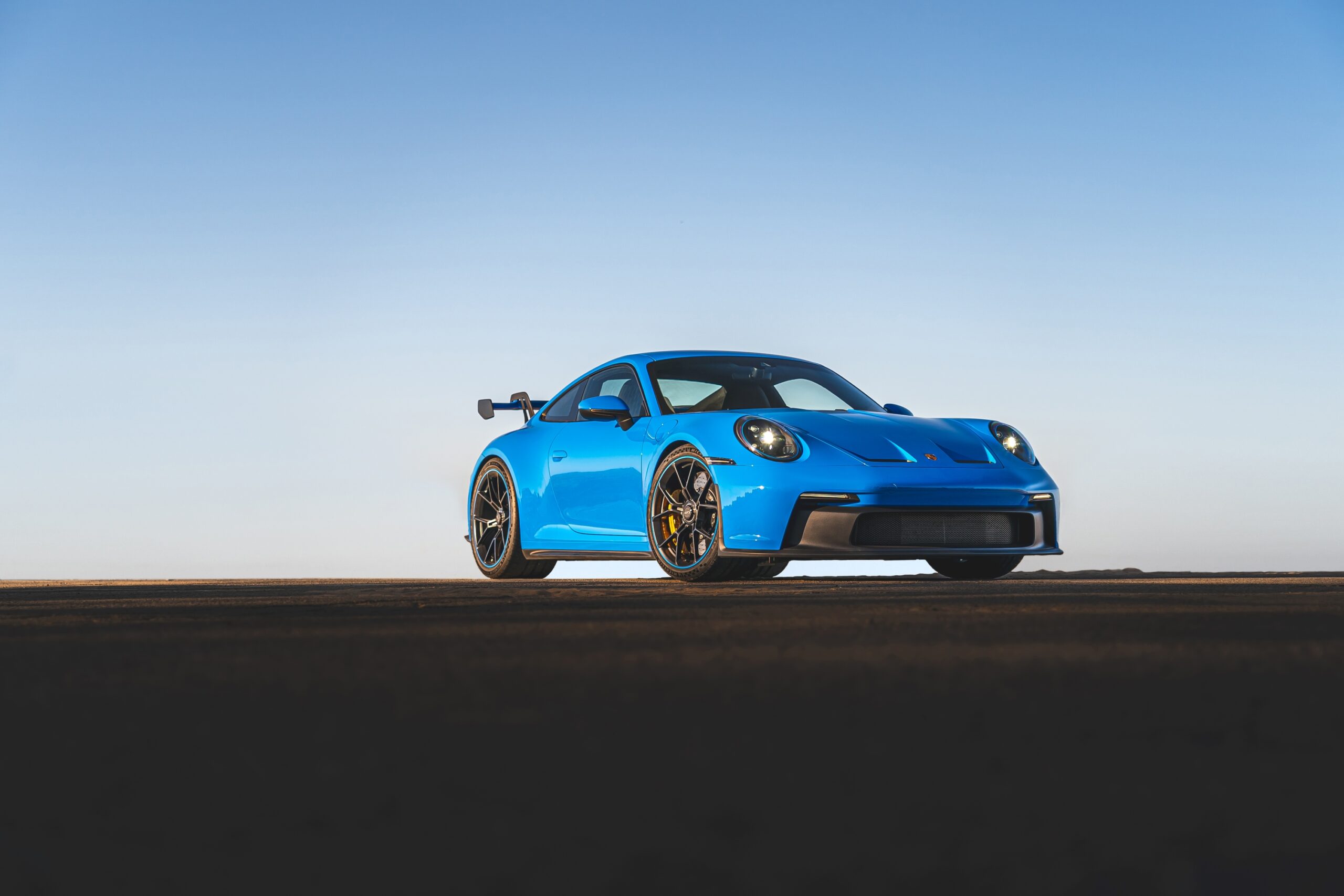 Blue sports car parked on a flat surface against a clear sky.