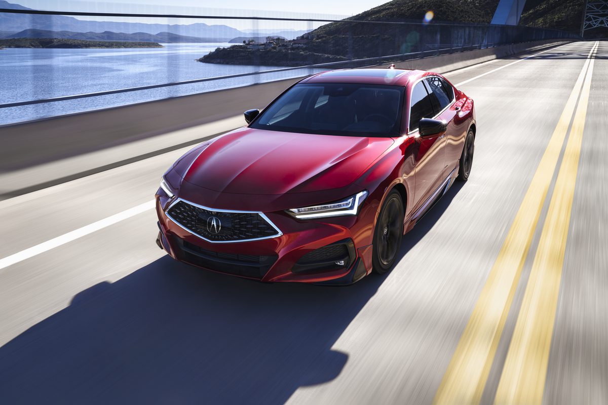 A sleek red luxury sports sedan driving on a coastal highway.
