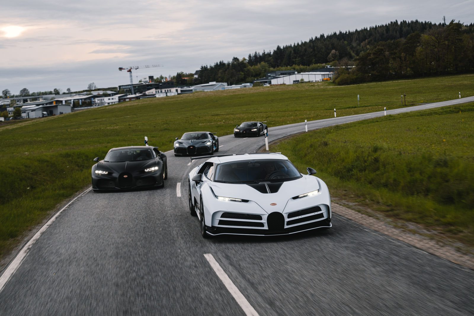 A white Bugatti Chiron leads a pack of luxury sports cars on a country road.