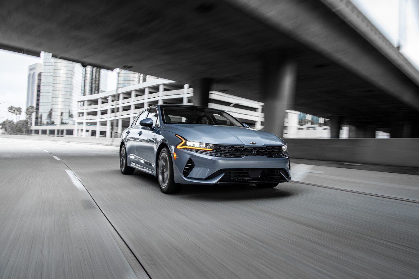 A sleek gray car driving under an urban overpass.