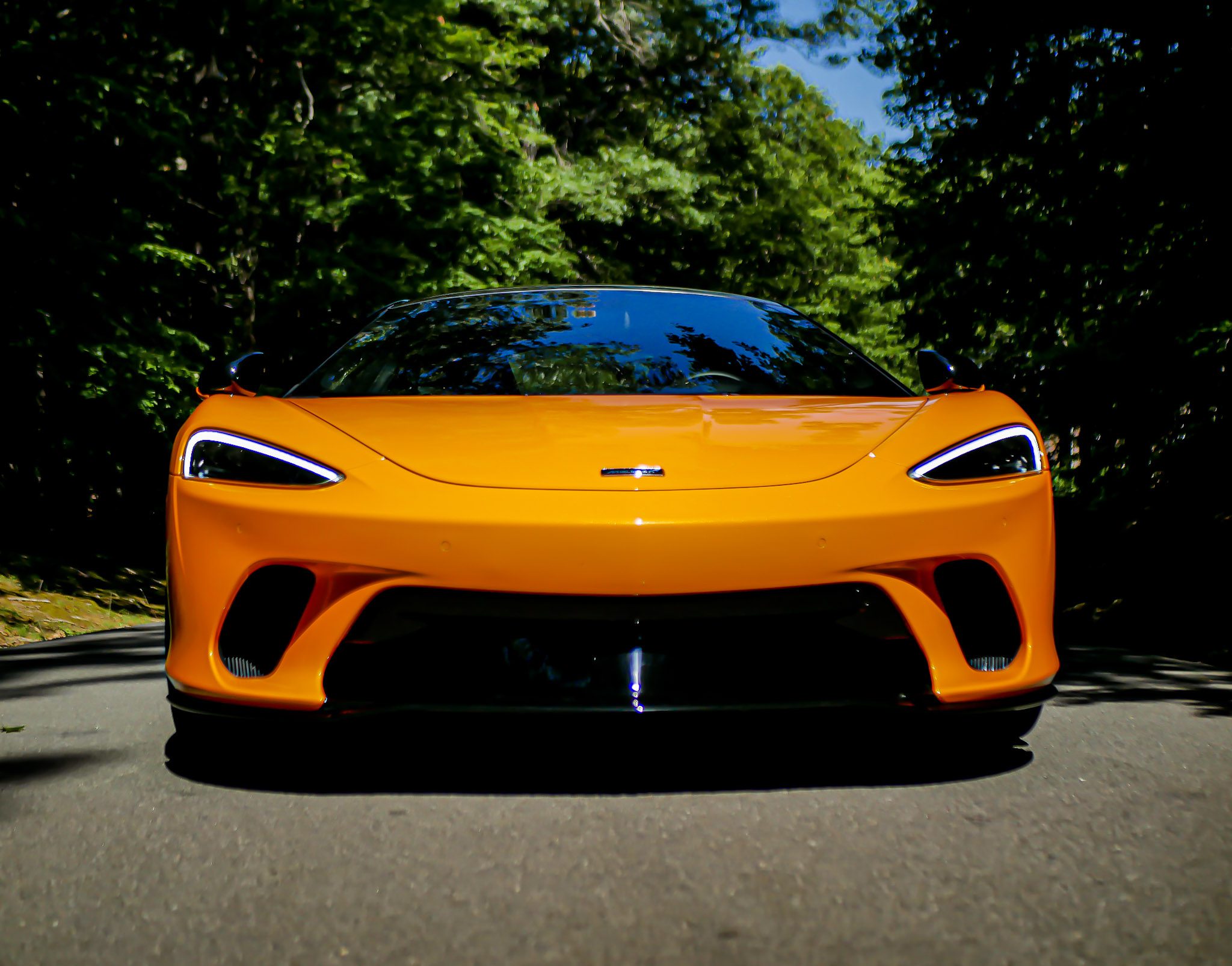Front view of a sleek orange sports car parked on a road surrounded by trees.
