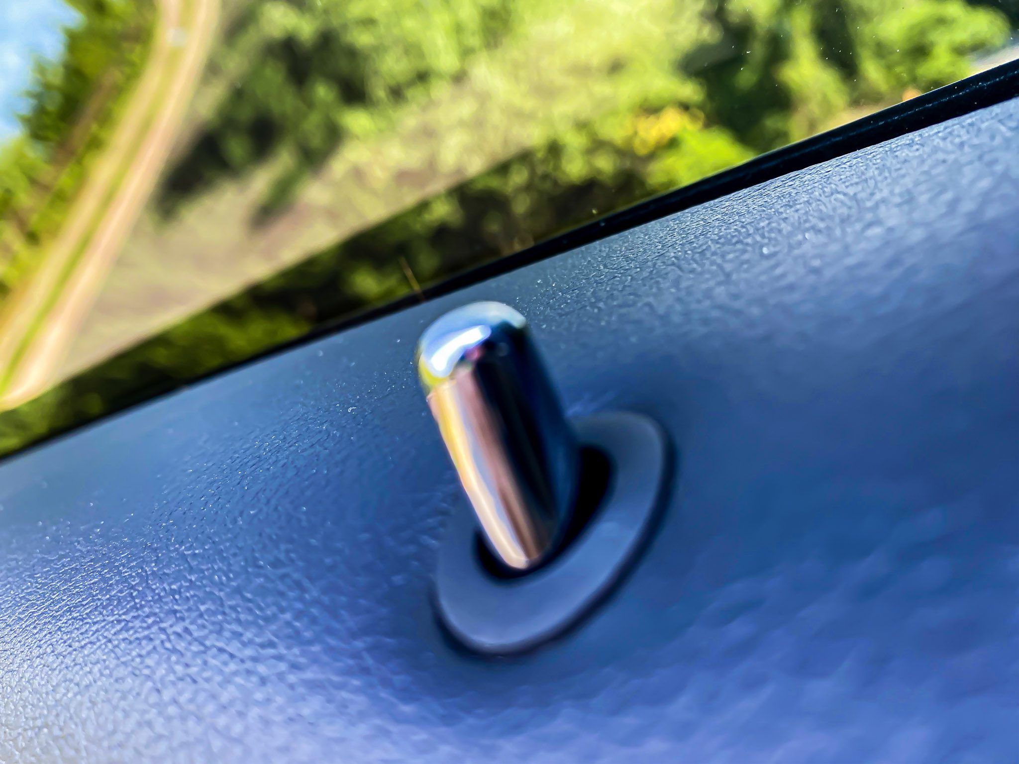 Close-up of a car door lock pin on a blue door panel.