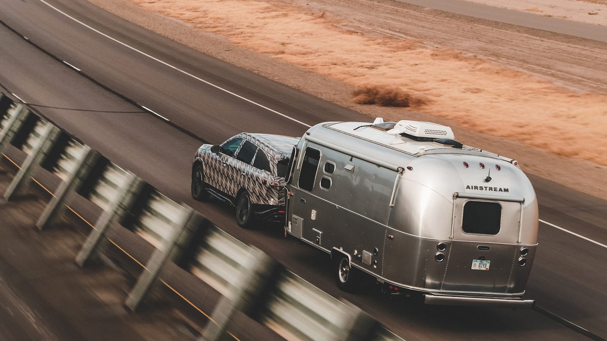 Car towing a classic silver camper trailer on a highway.
