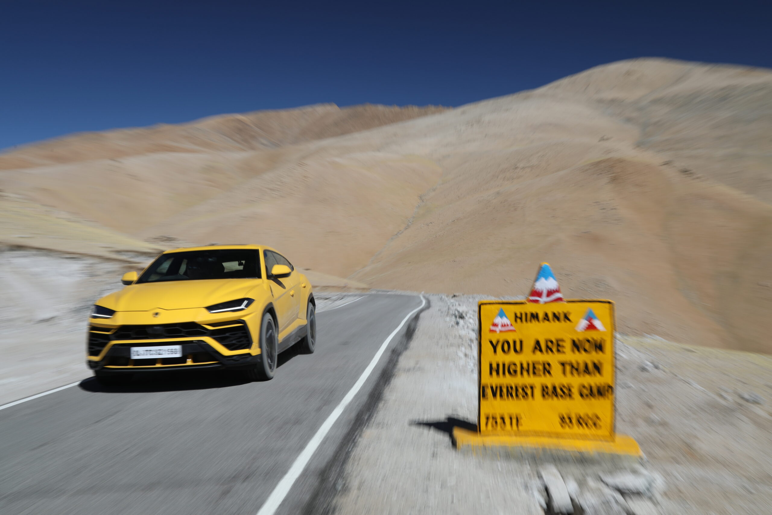 Yellow sports car driving on a mountain road with a warning sign.