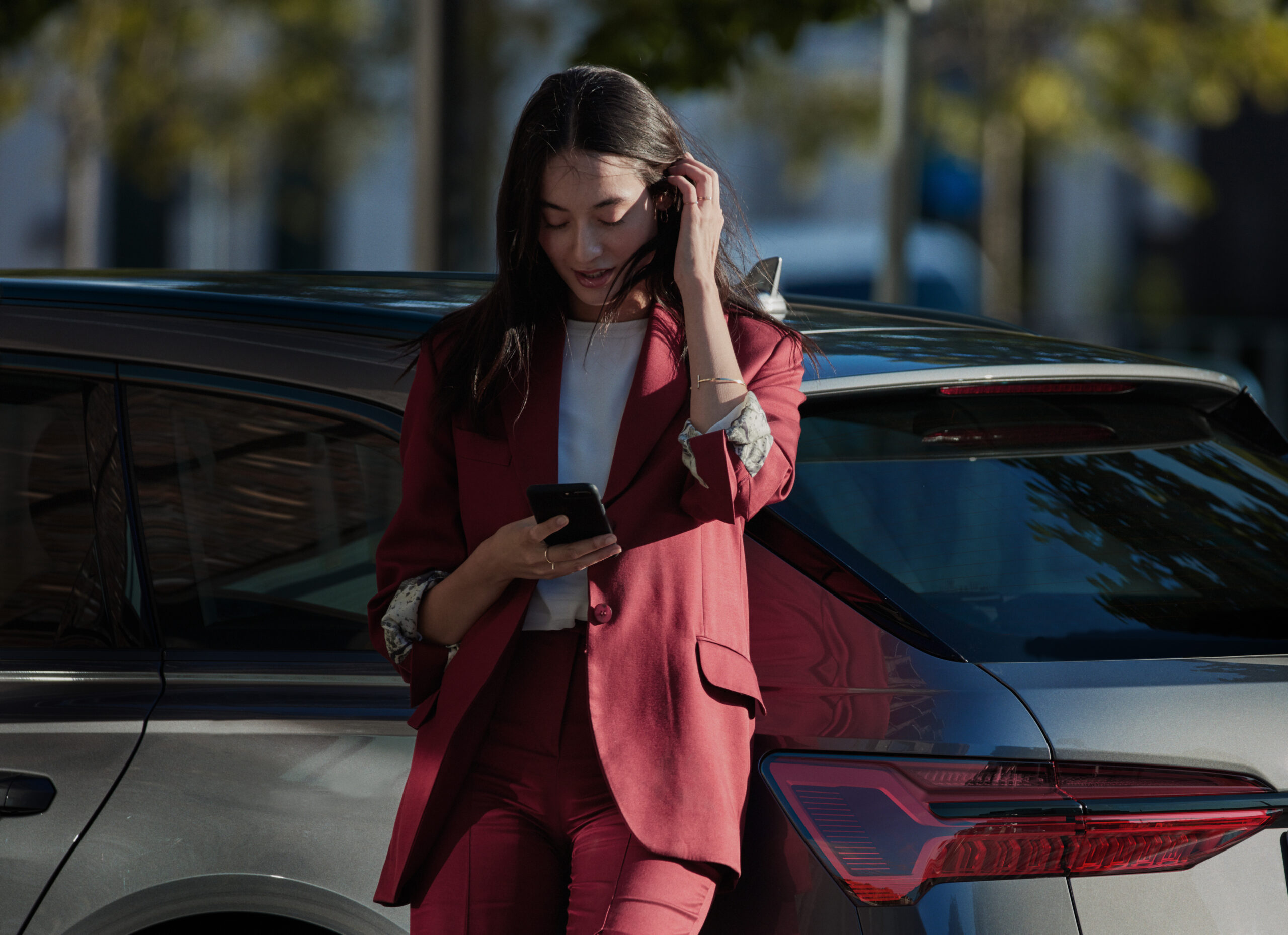 Woman in red suit using phone near a car outdoors.