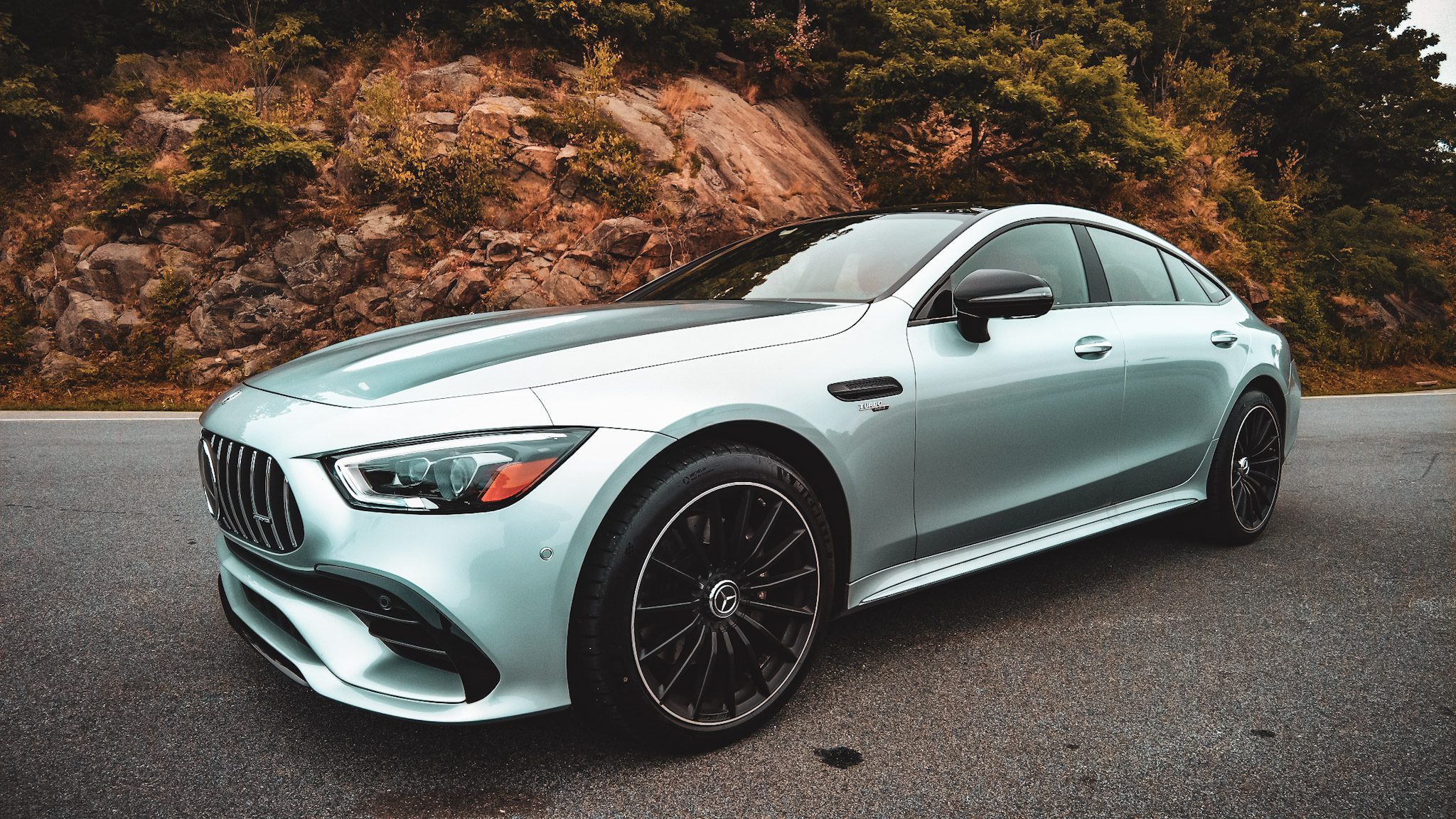 Sleek mint green luxury car parked on a road with autumn foliage.