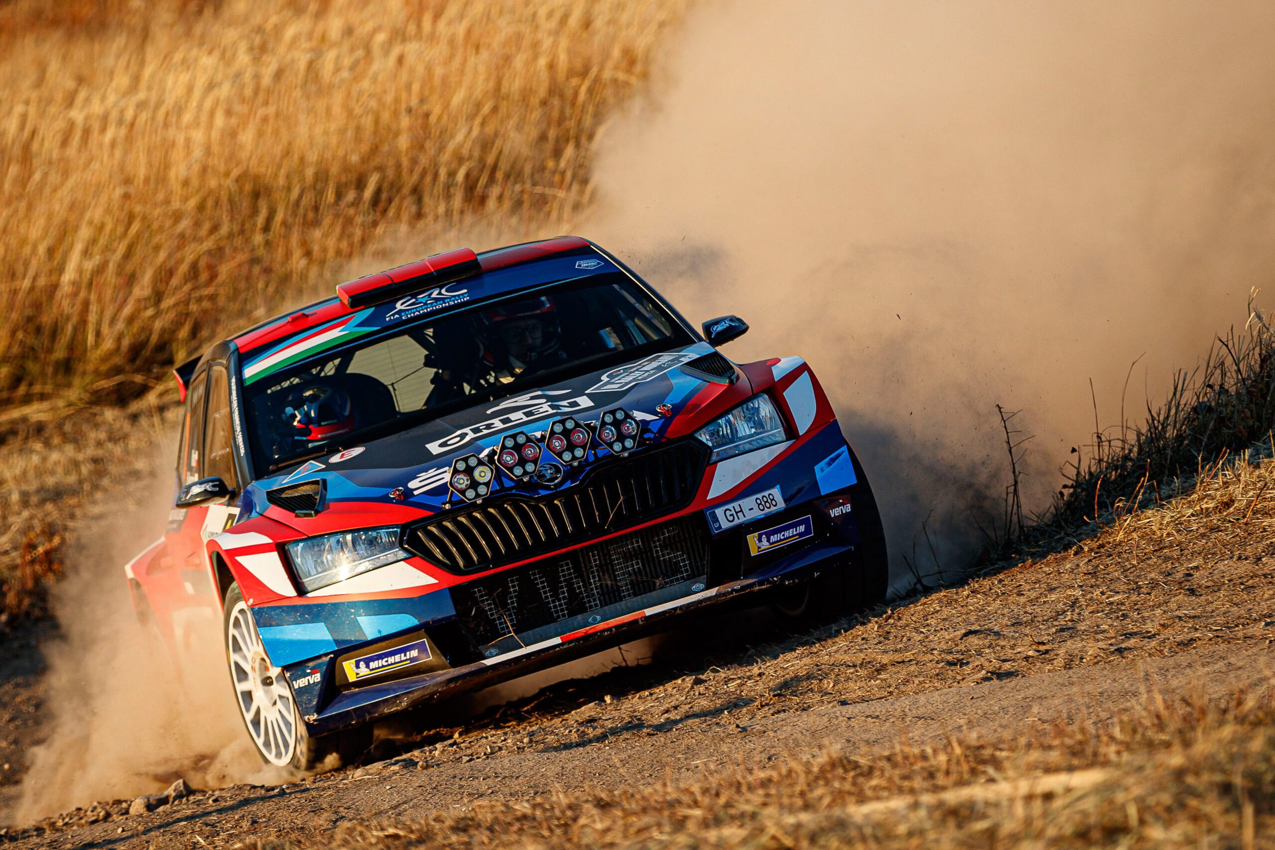 Rally car kicking up dirt on a rugged track.