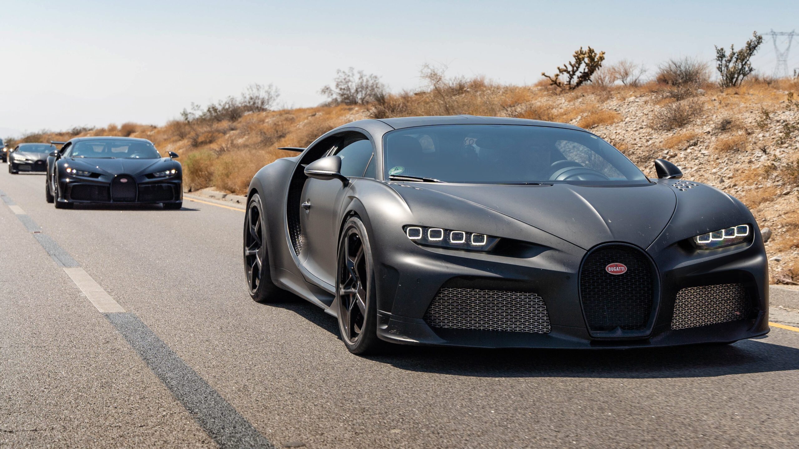Matte black Bugatti sports car parked on a desert road.