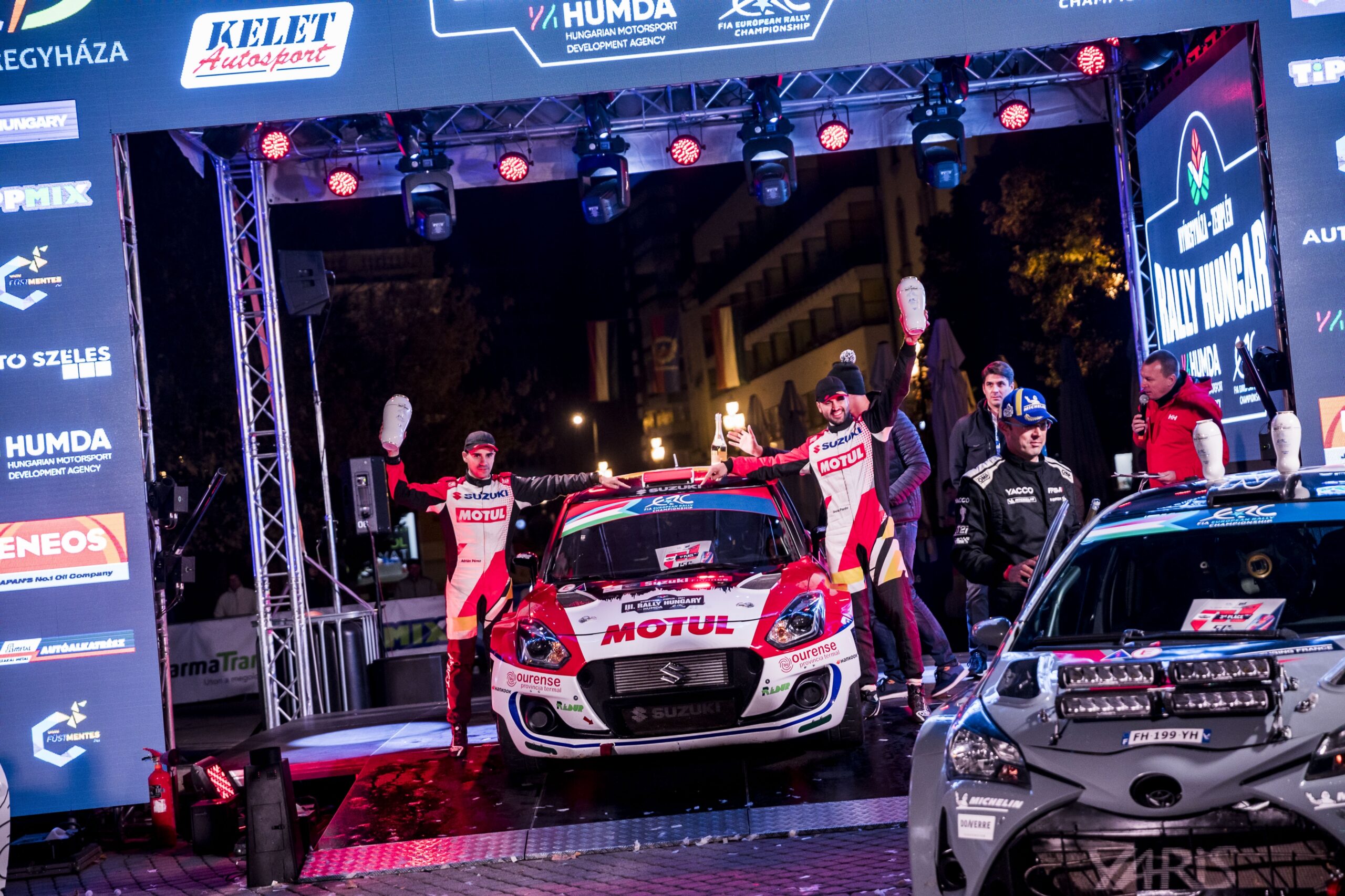 Rally car and team celebrating on stage at night event.