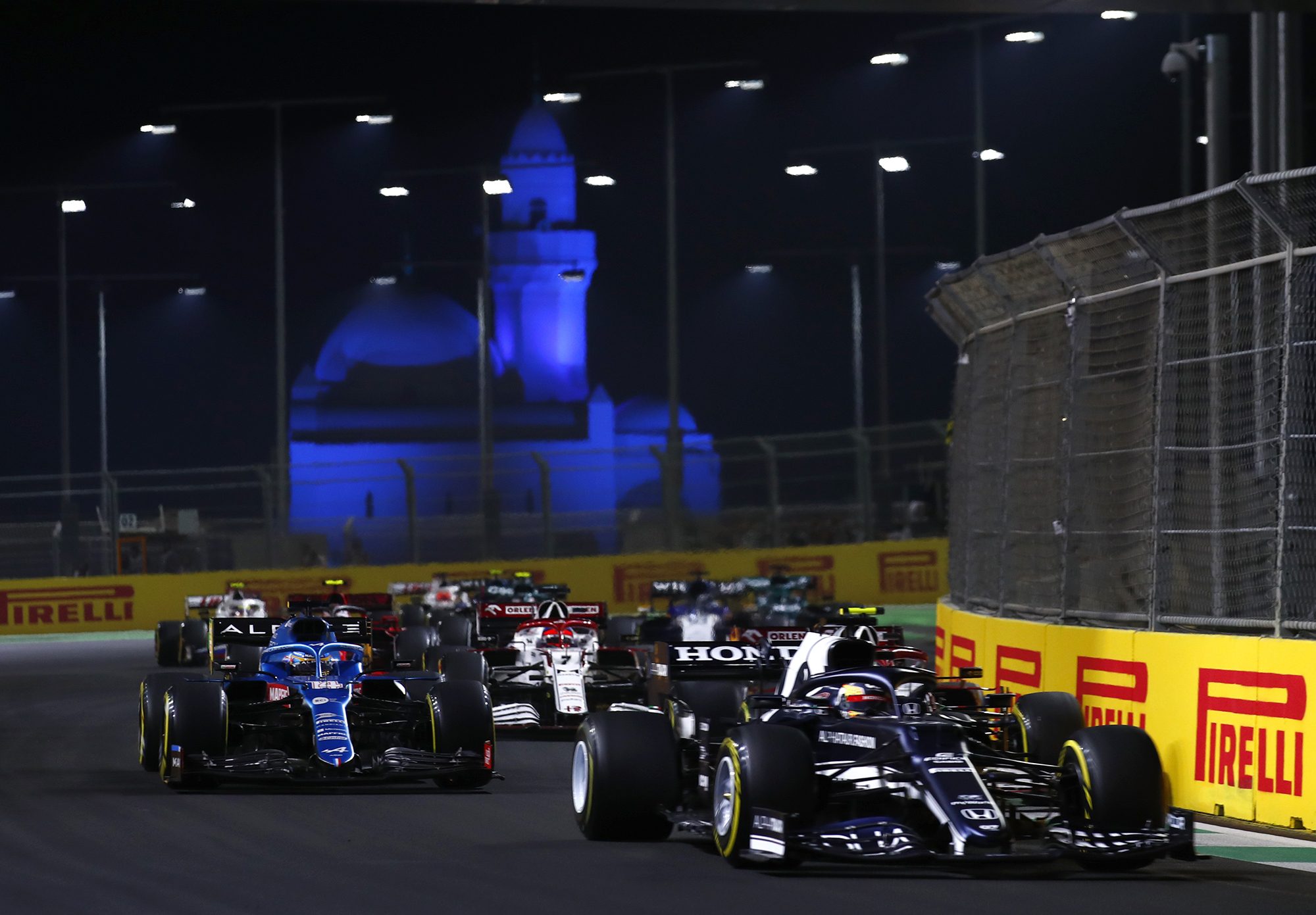Formula 1 cars race at night with a lit castle in the background.