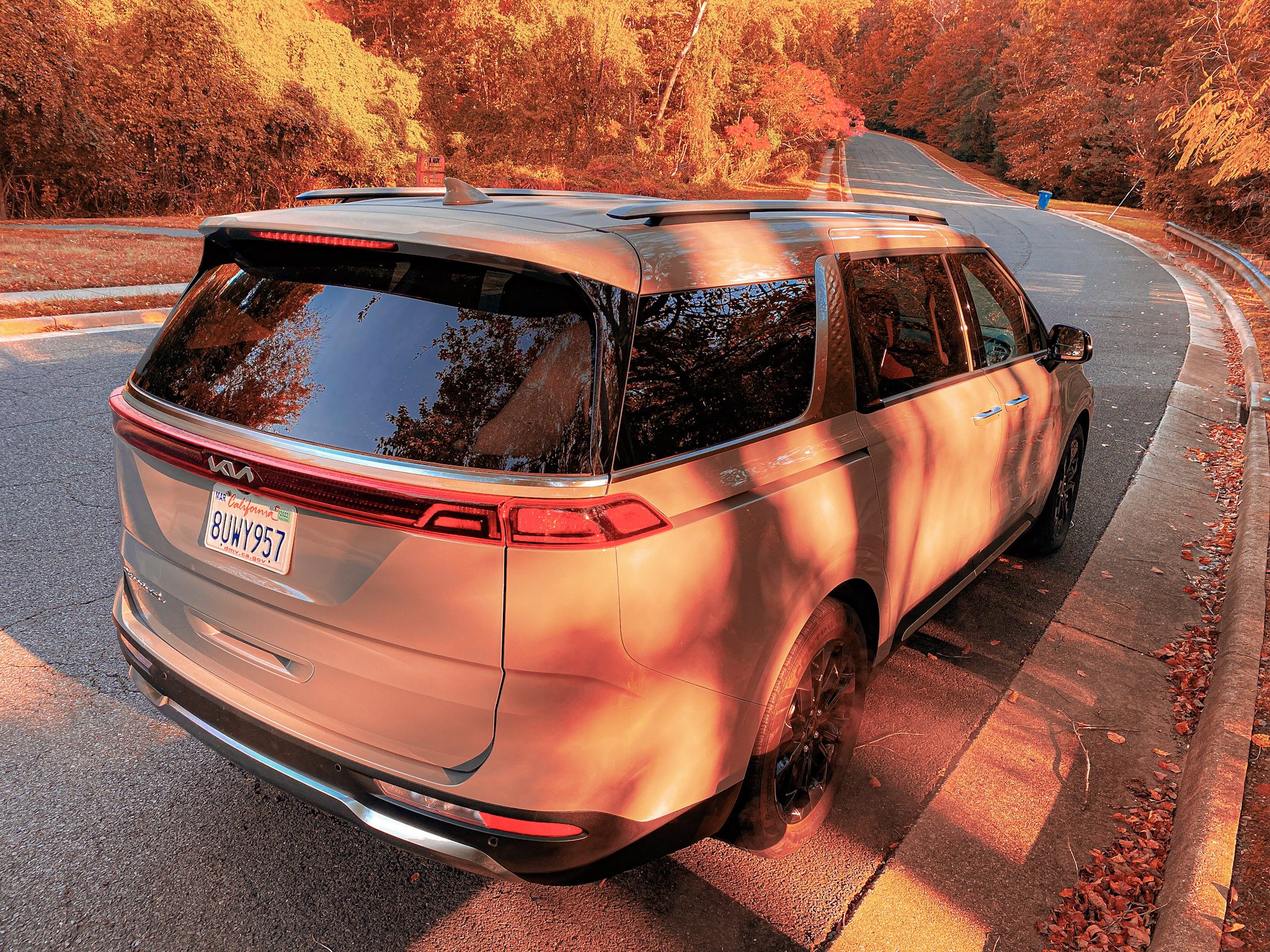 Sunset-lit modern SUV parked on a road surrounded by autumn trees.