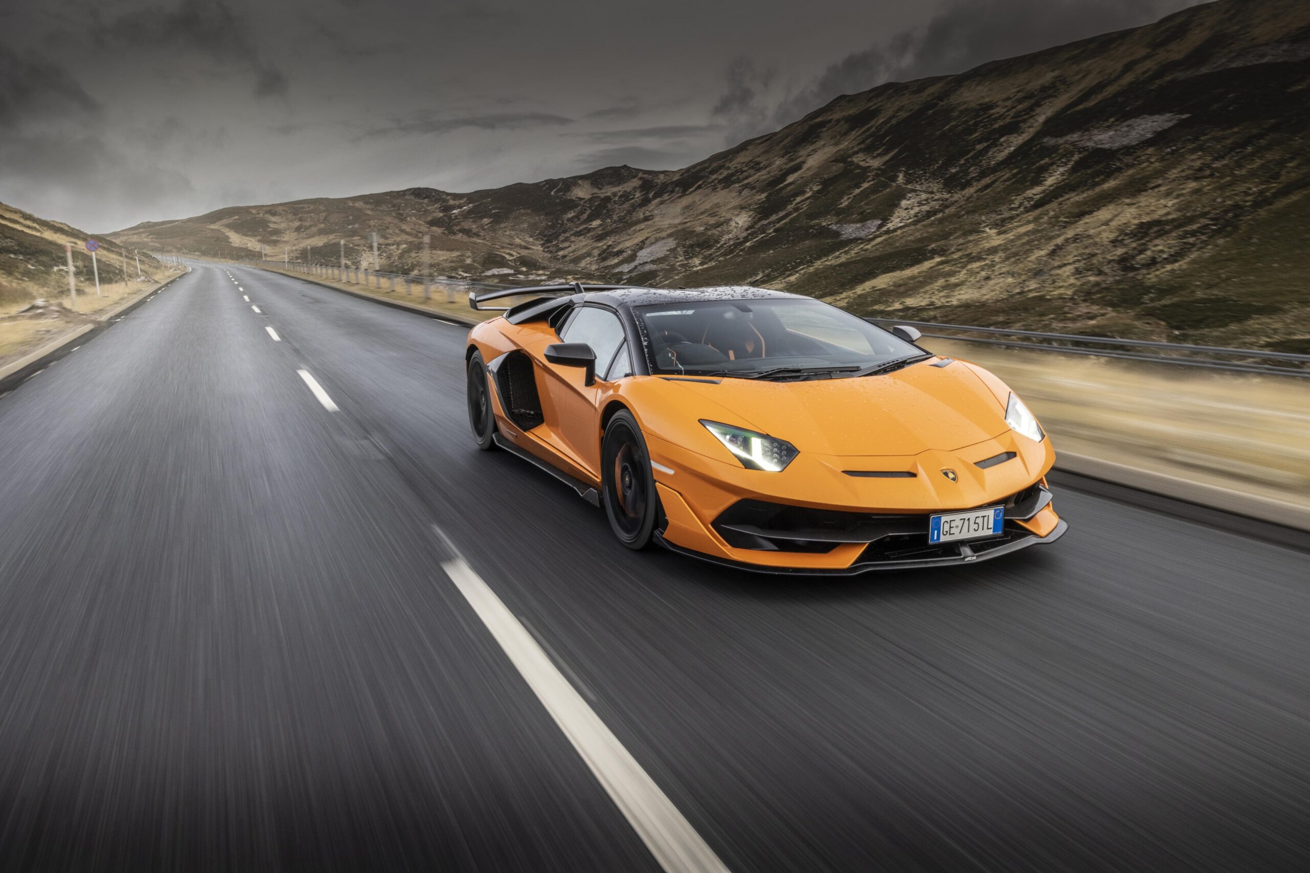 Orange sports car speeding on a mountain road.