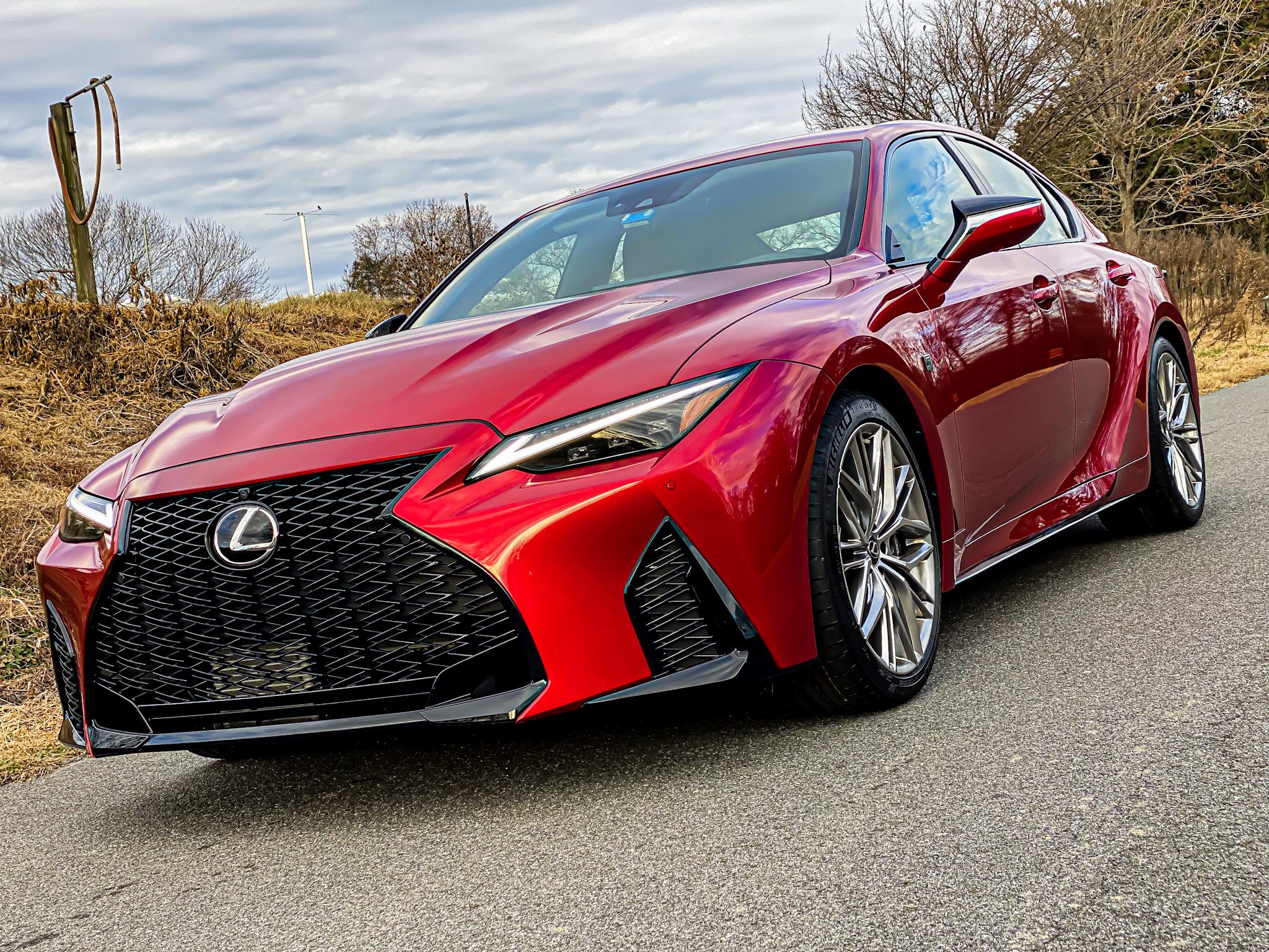 A shiny red Lexus sports car parked on a road under a cloudy sky.