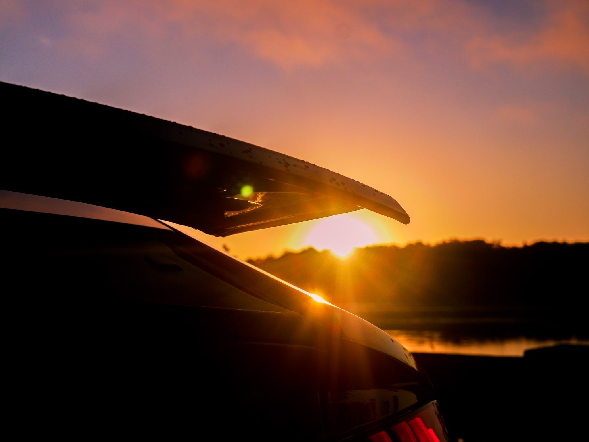 Car spoiler silhouetted against a vibrant sunset sky.
