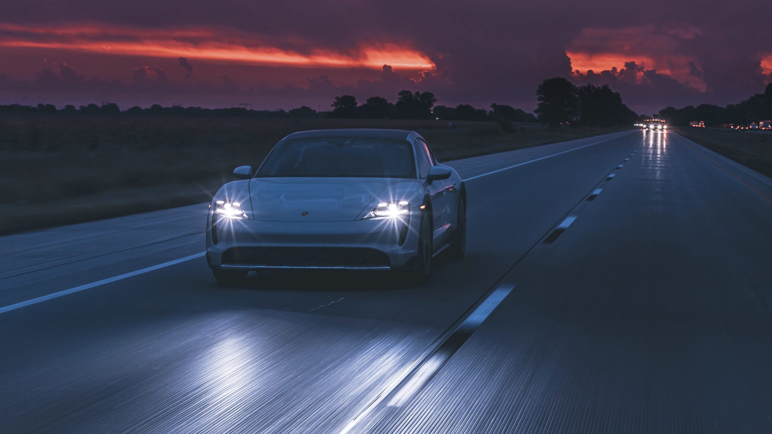 Electric car driving on a highway at dusk with headlights on.