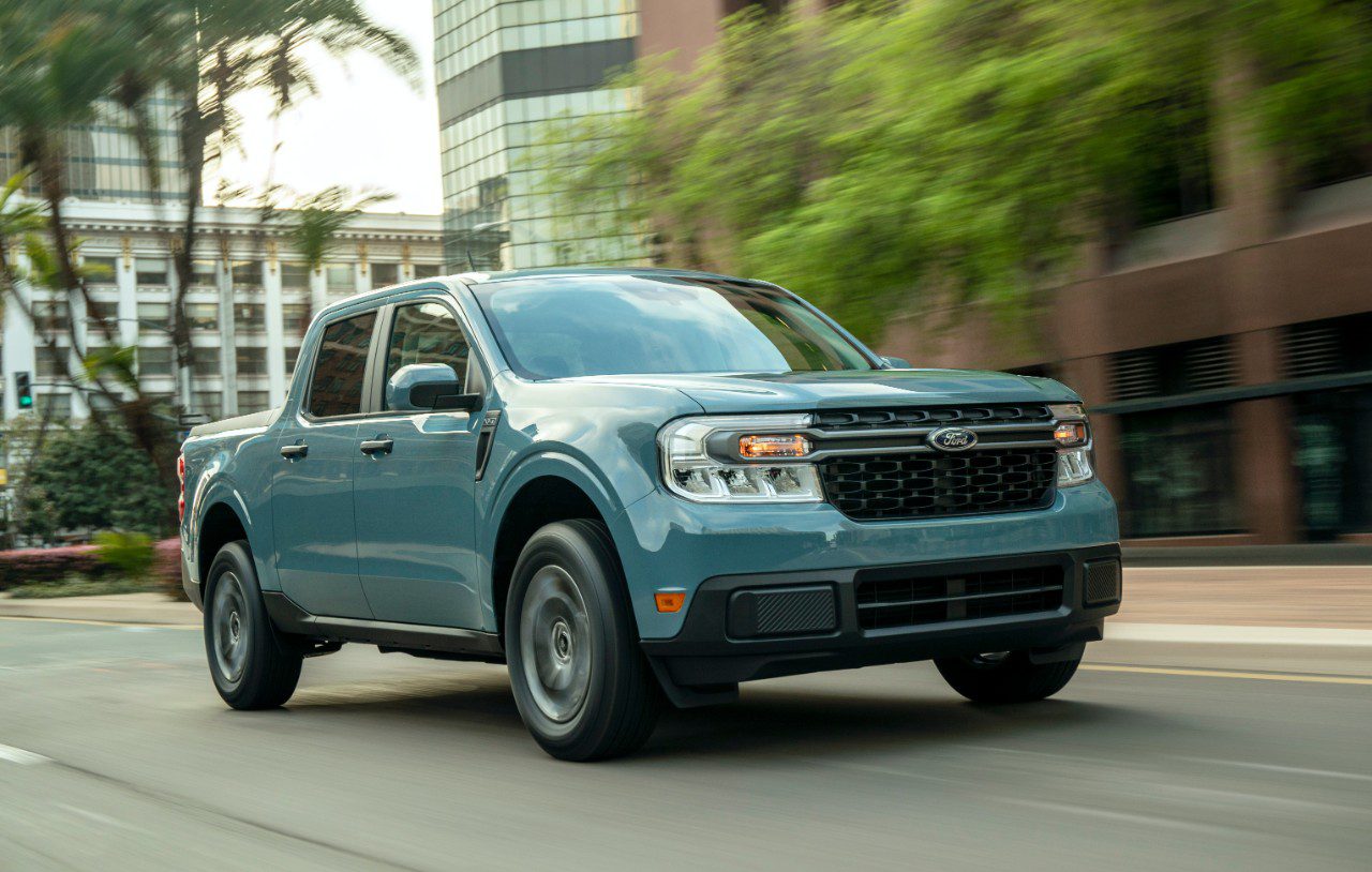 A blue SUV drives on a city street with buildings in the background.