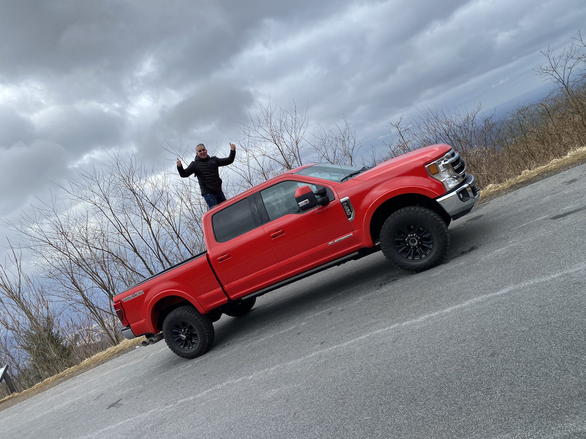 Person standing on a red pickup truck on a roadside.