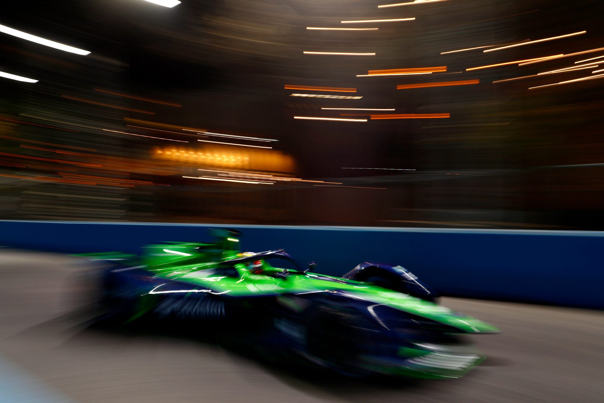 Blurred green and blue racing car speeding on a track at night.