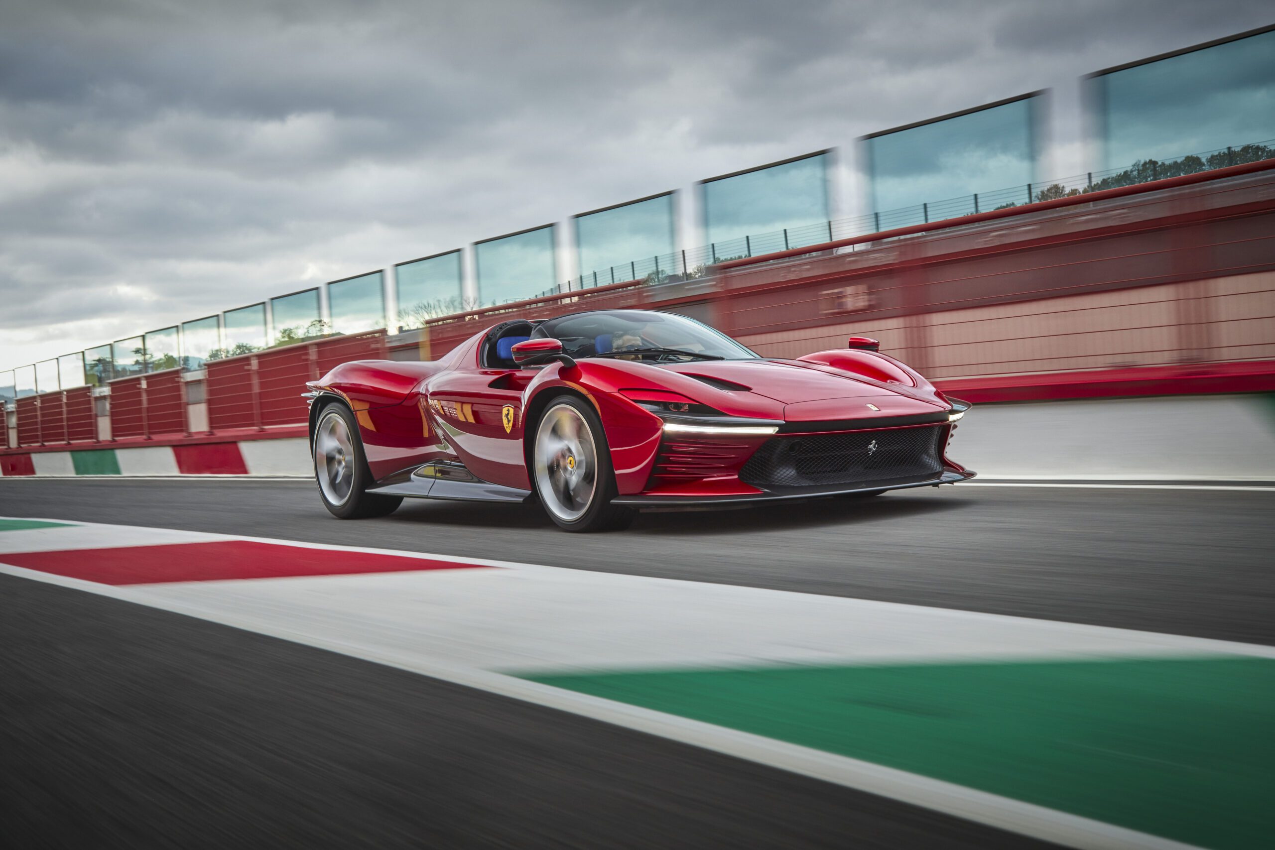 A sleek red sports car speeding on a race track under a cloudy sky.