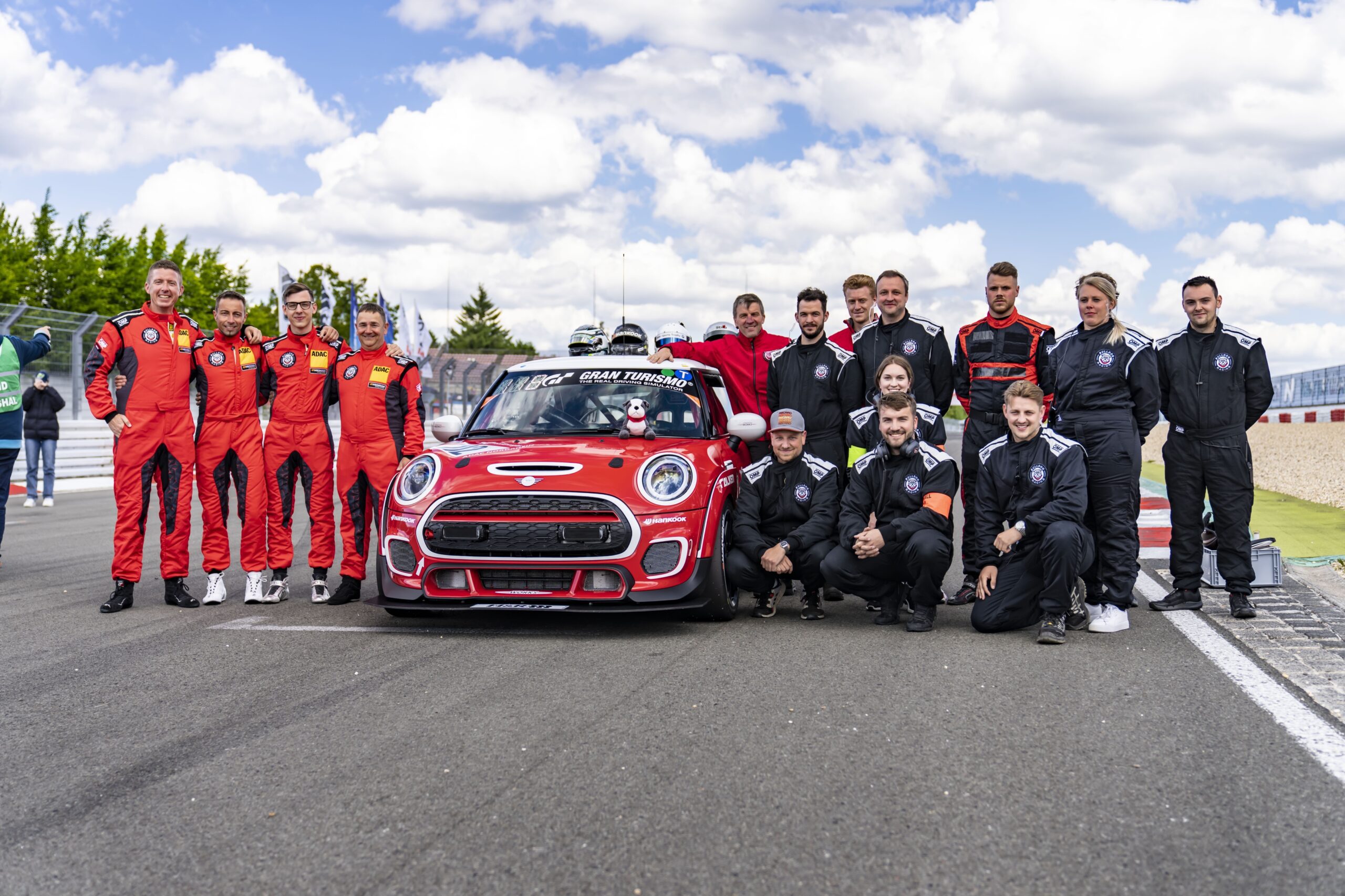 Racing team posing with a red Mini Cooper on track.
