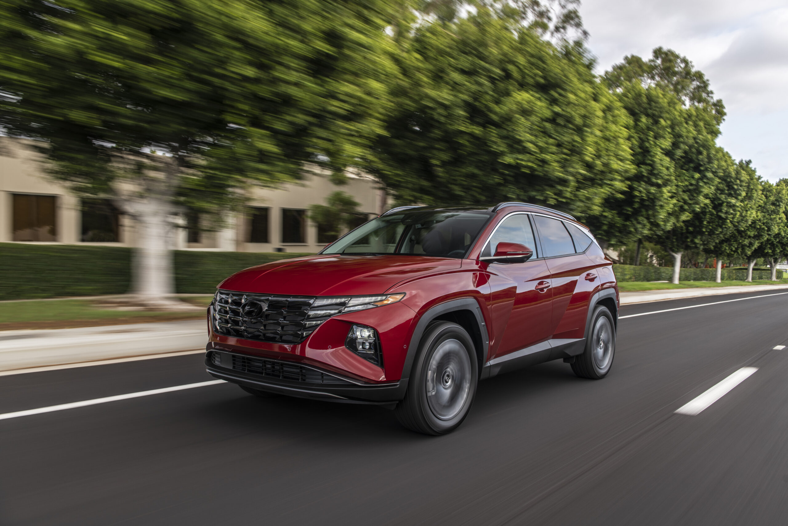 A red SUV driving on a tree-lined street.
