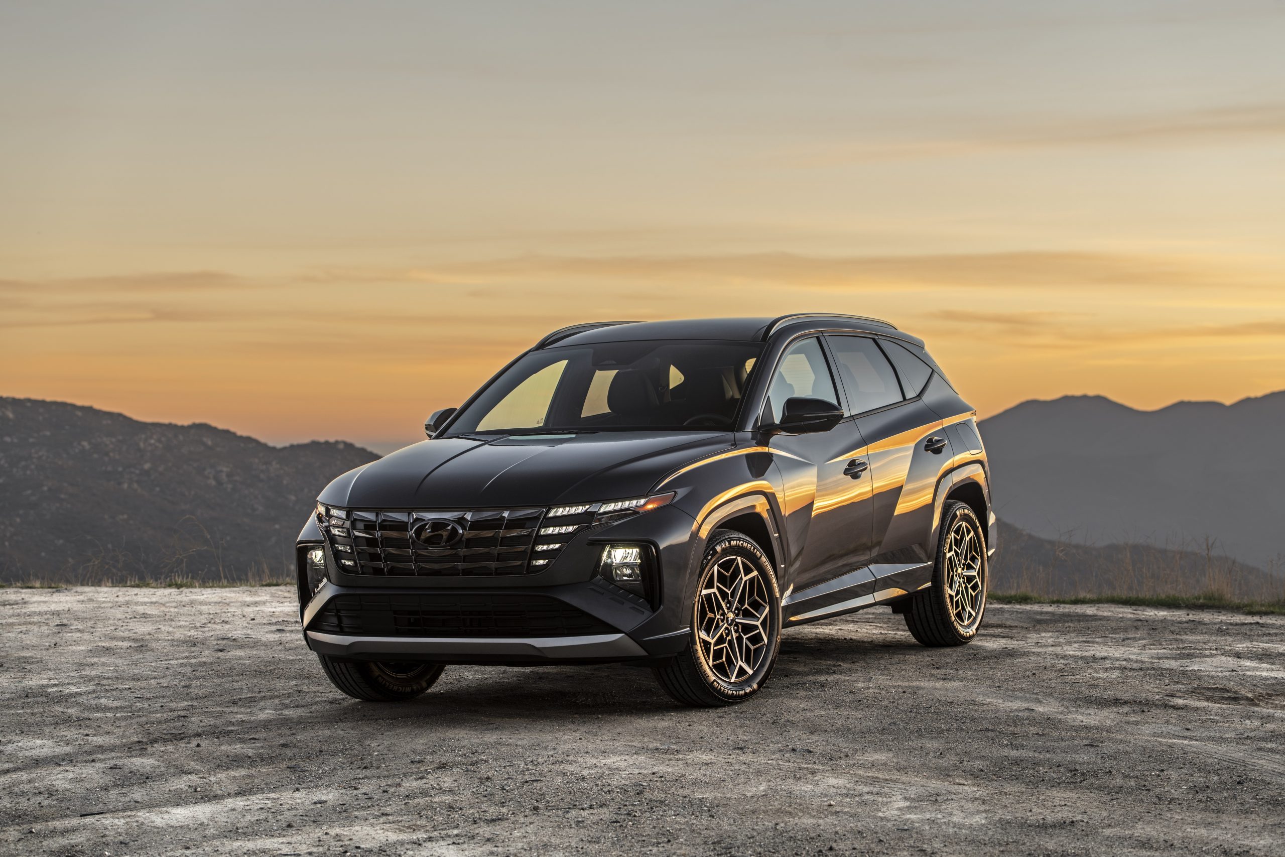 A sleek black SUV parked on a dirt road during sunset.