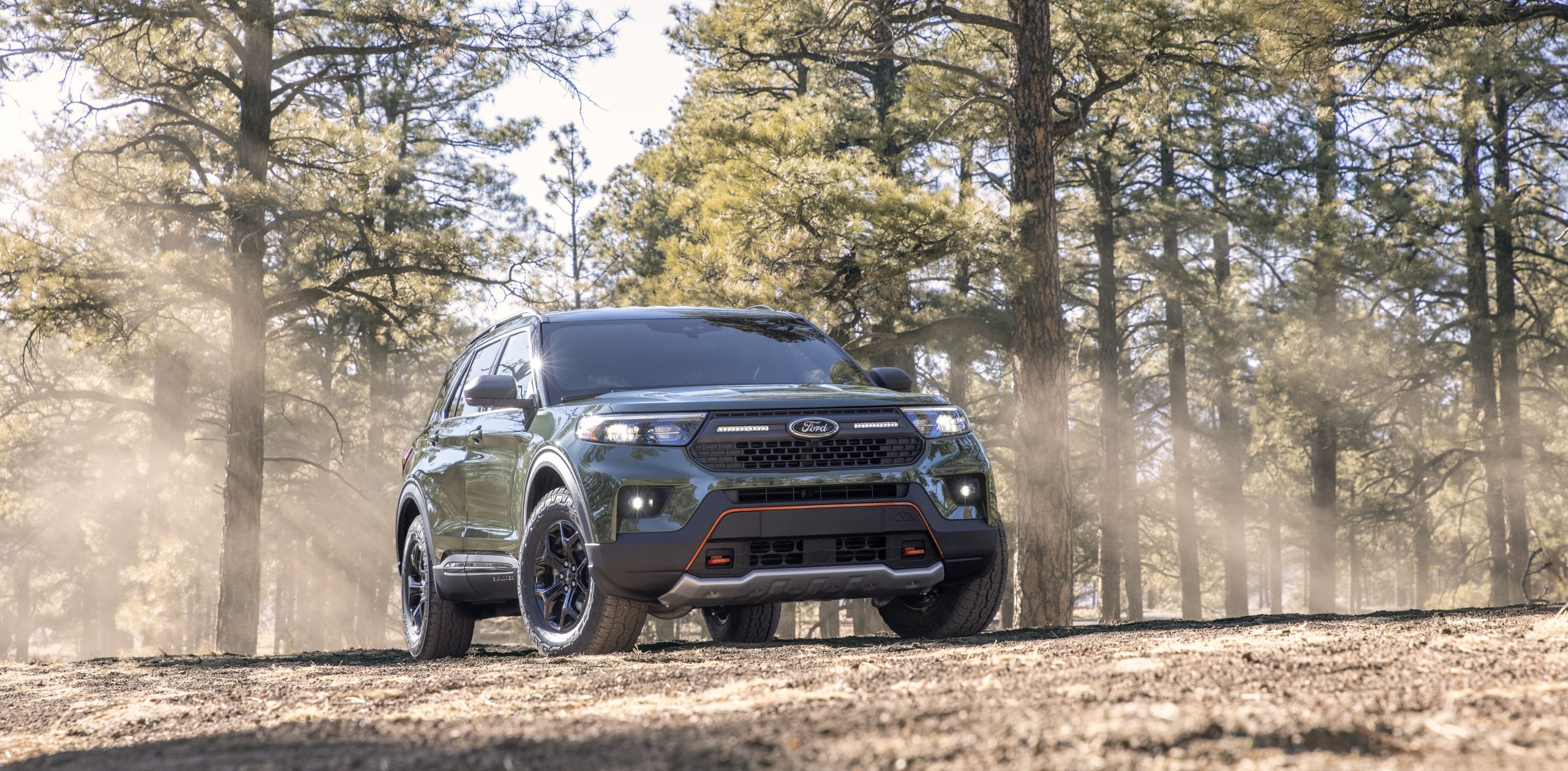 A rugged SUV driving through a forest trail kicking up dust.
