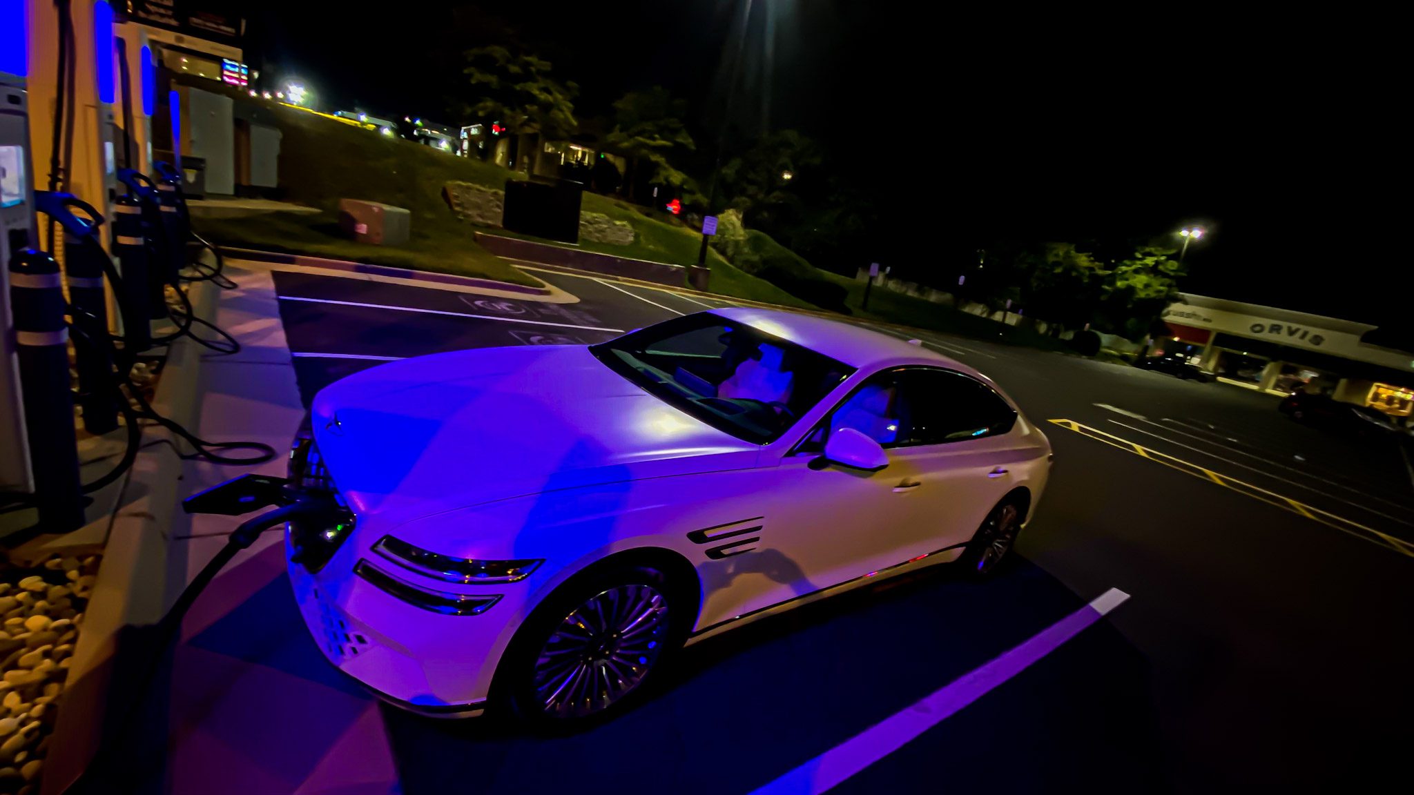 White luxury car parked at night under streetlights in a lot.