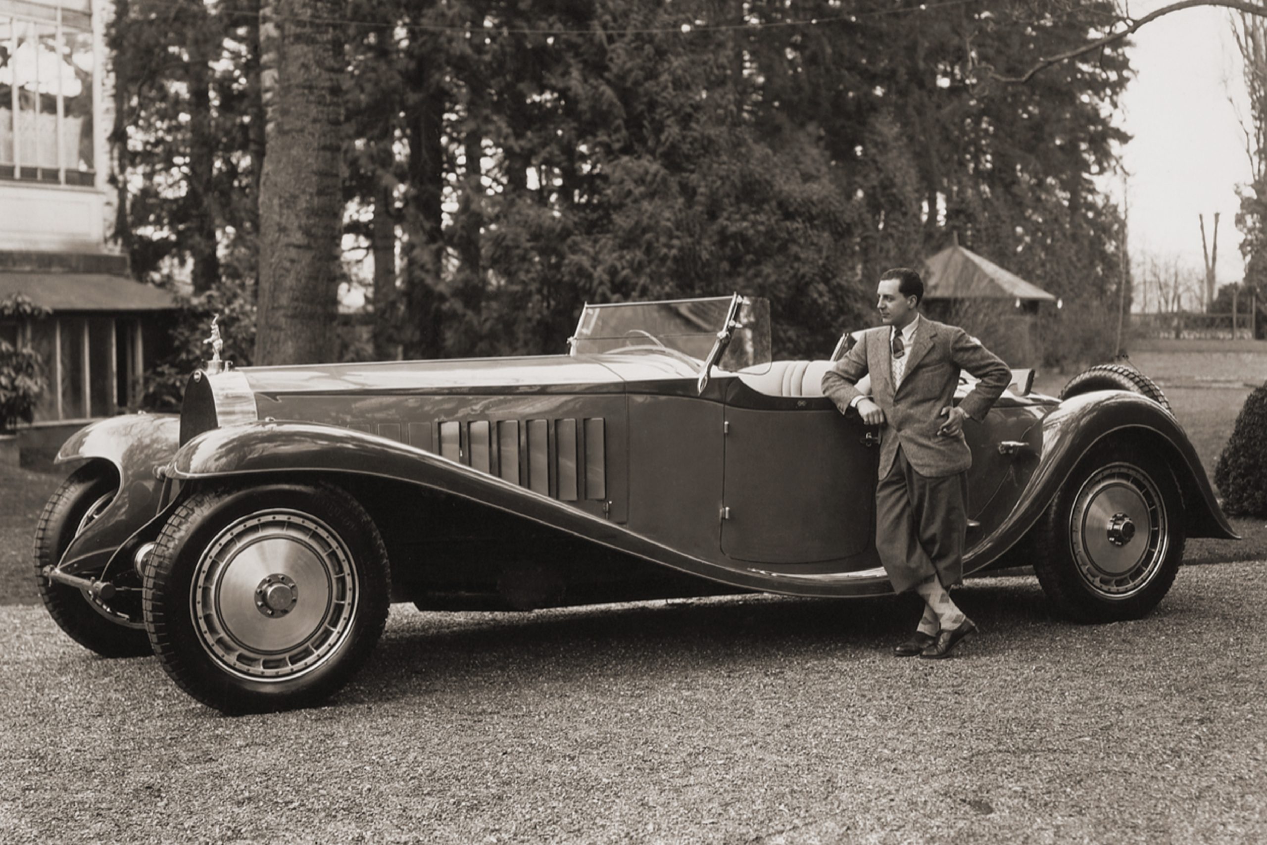 Vintage photo of a man leaning on a classic luxury car by the forest.